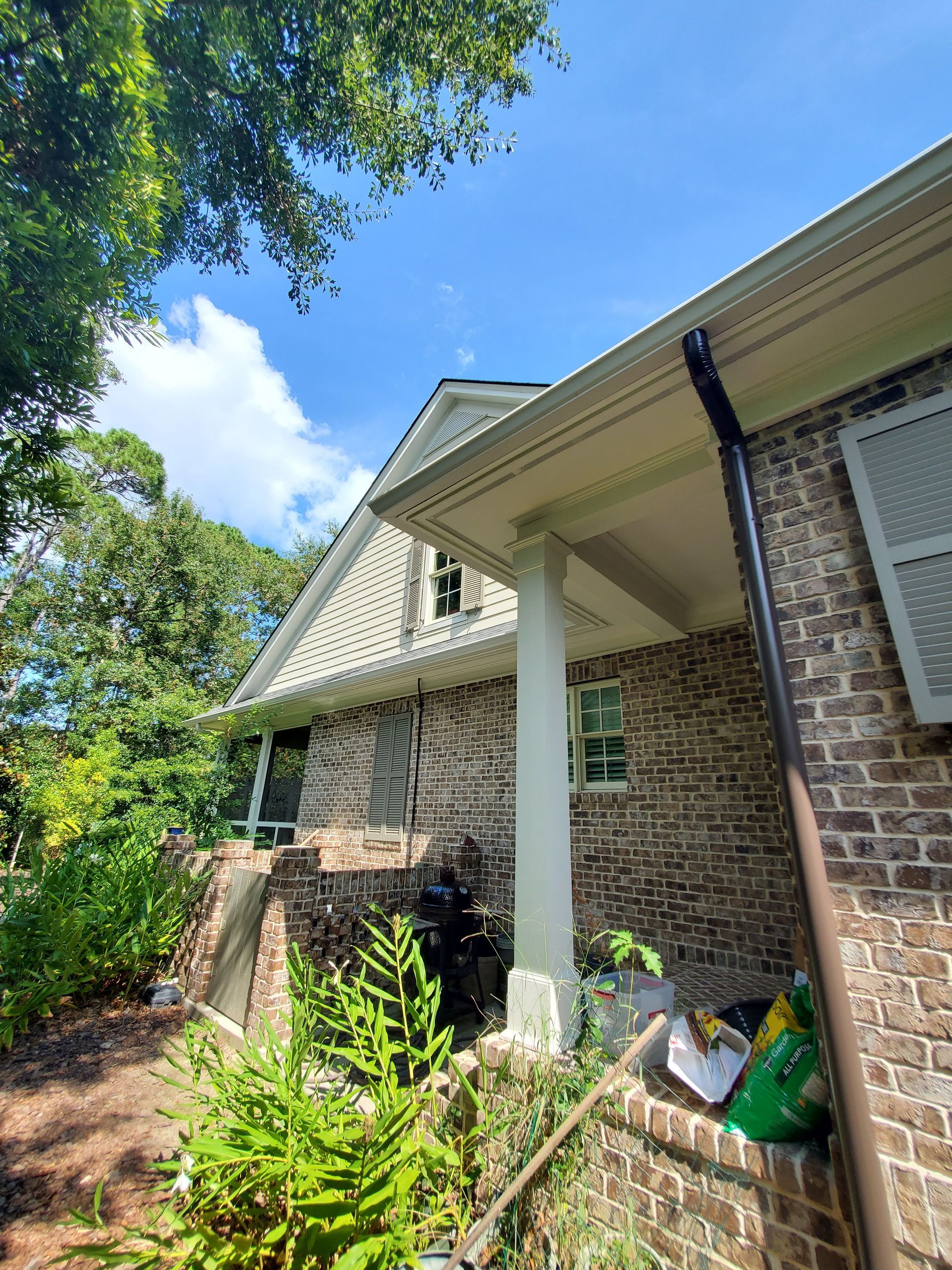 Brick house exterior with white trim, porch, and dark gutters against a blue sky.