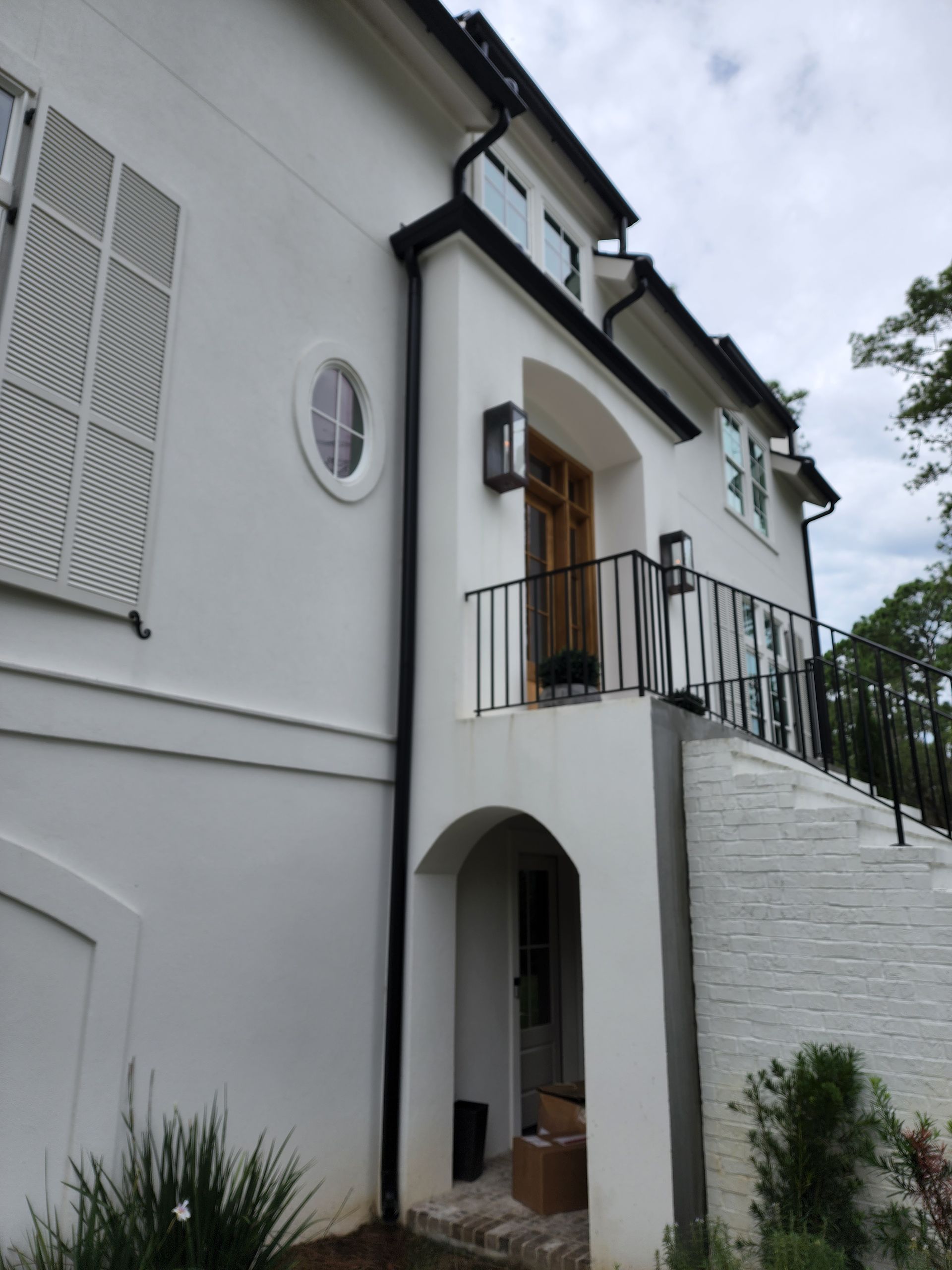 White house exterior with shutters, arched doorway, black gutters, and iron railing.