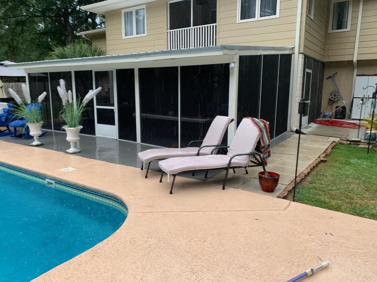 Poolside patio with screened enclosure, lounge chairs, and two-story house with tan siding.