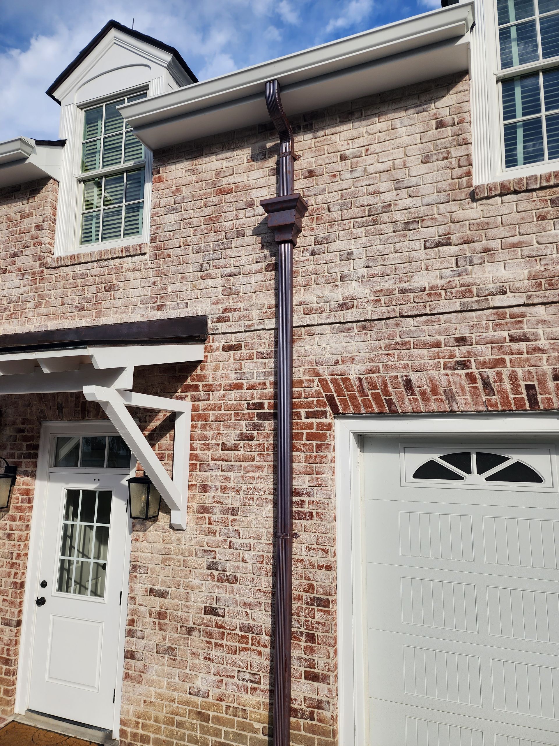 Brick building with a white door, garage, and windows. Brown downspout runs vertically.
