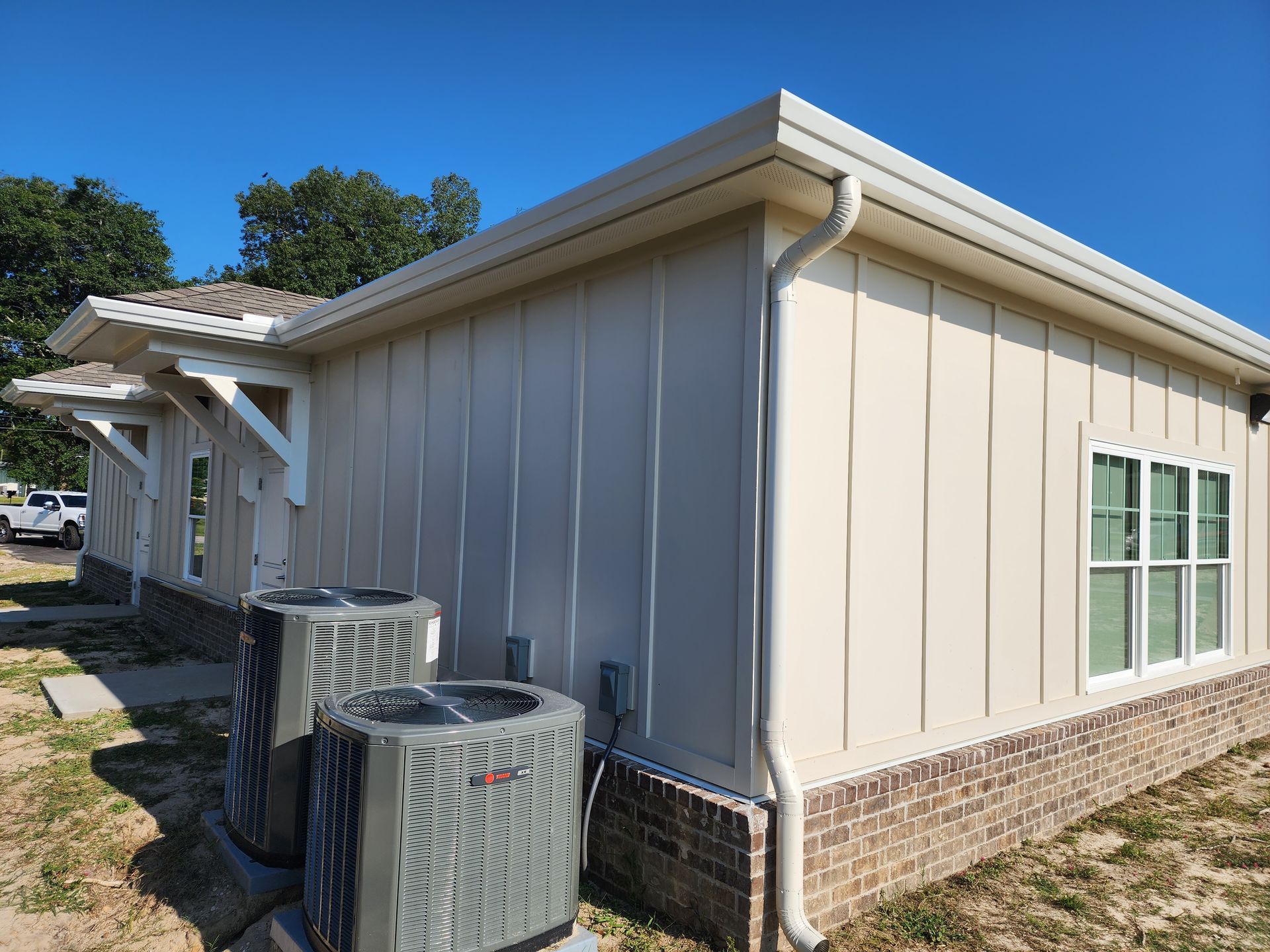 Beige sided building with white trim, gutters, and windows. Two air conditioning units sit in front.