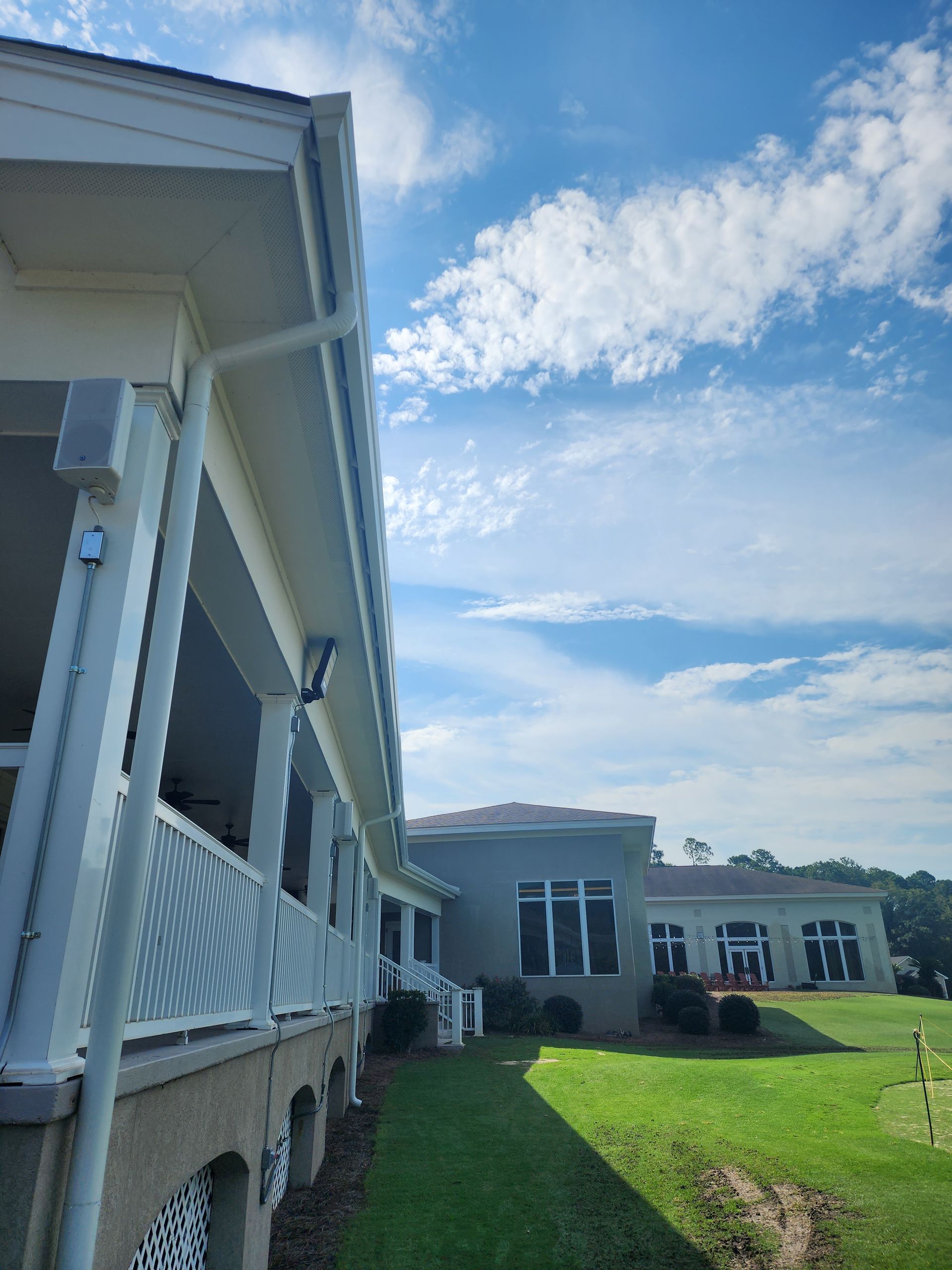 White building with a porch, green grass, and a sunny, cloudy sky.