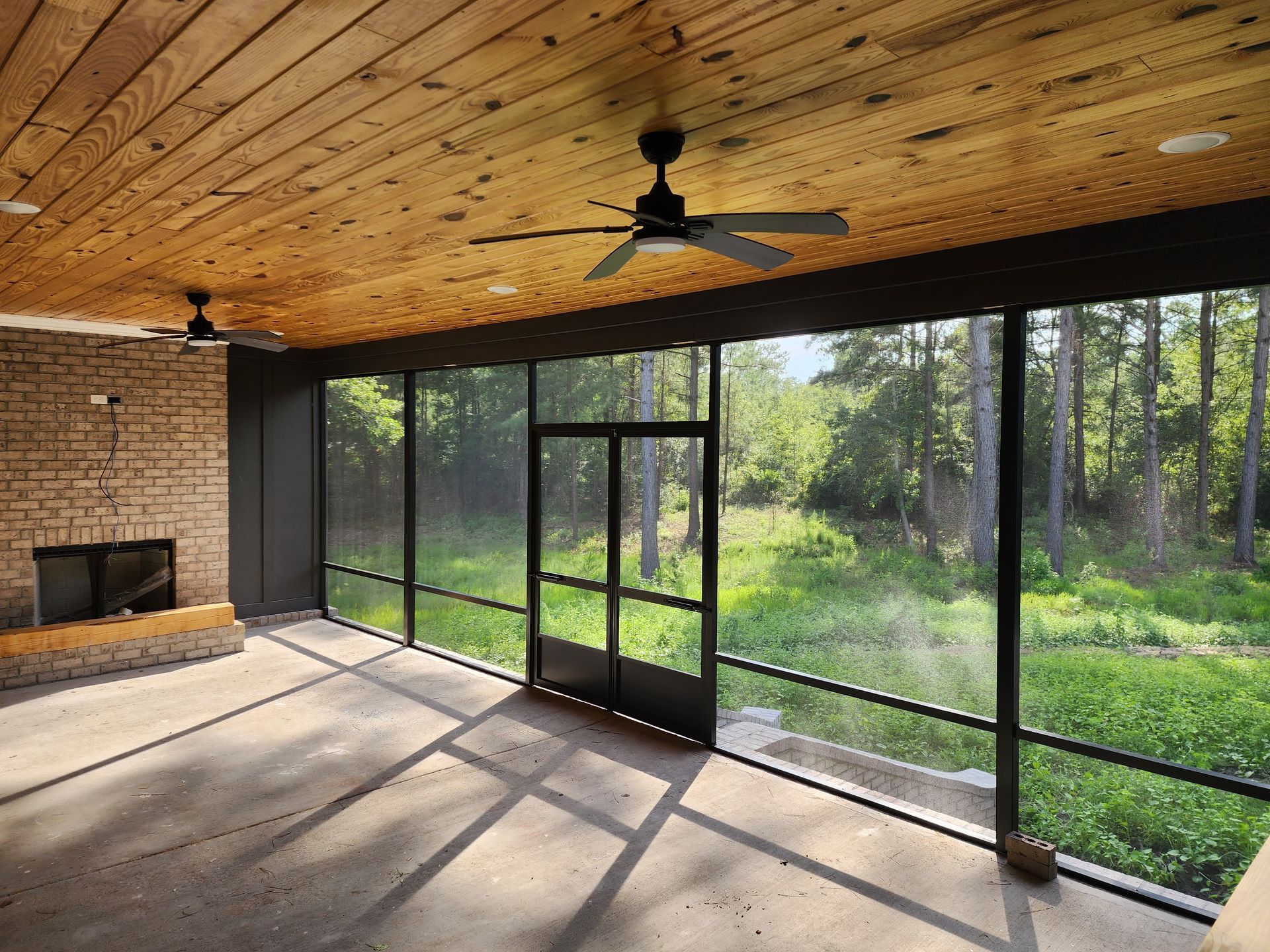 A screened in porch with a ceiling fan and a fireplace