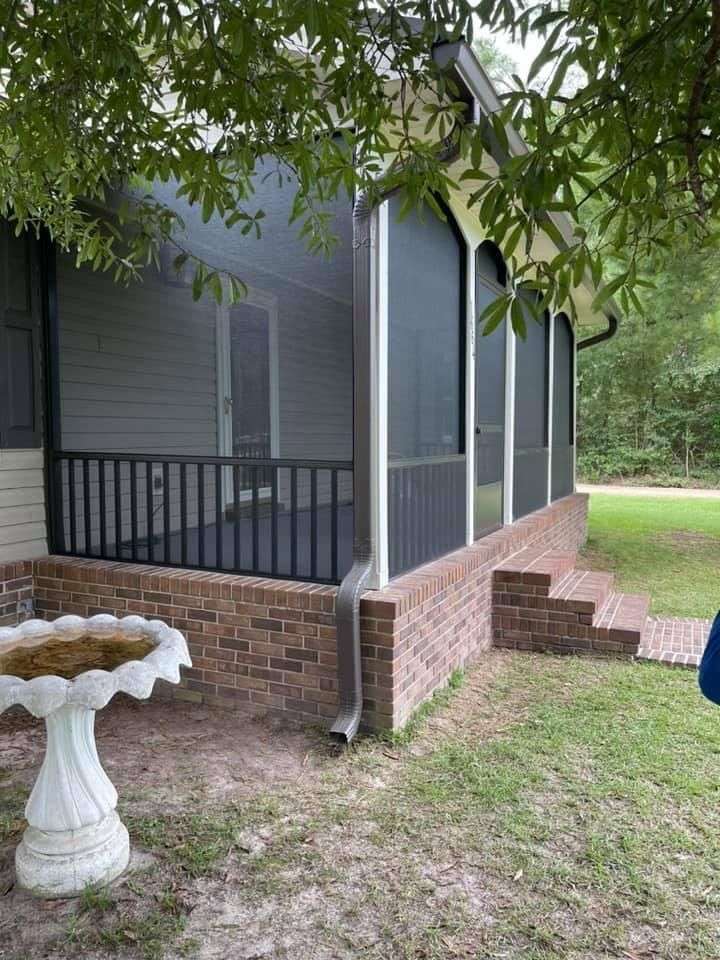 Screened porch with brick base and black railing. White birdbath in front.
