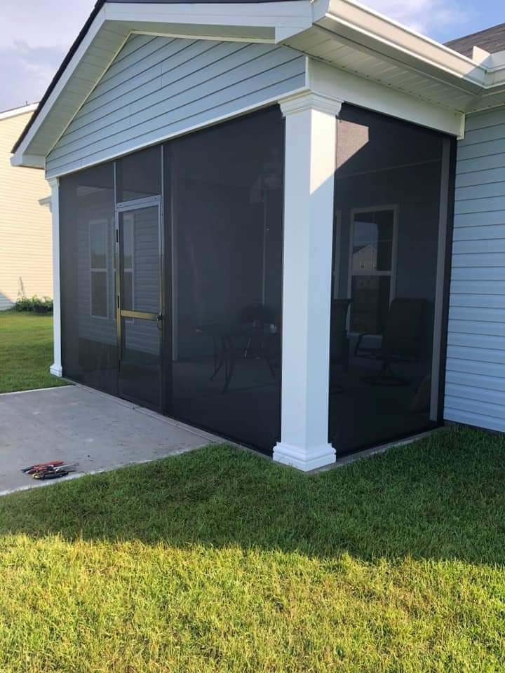 Screened-in porch attached to a house with black screens, white columns, and a concrete patio.