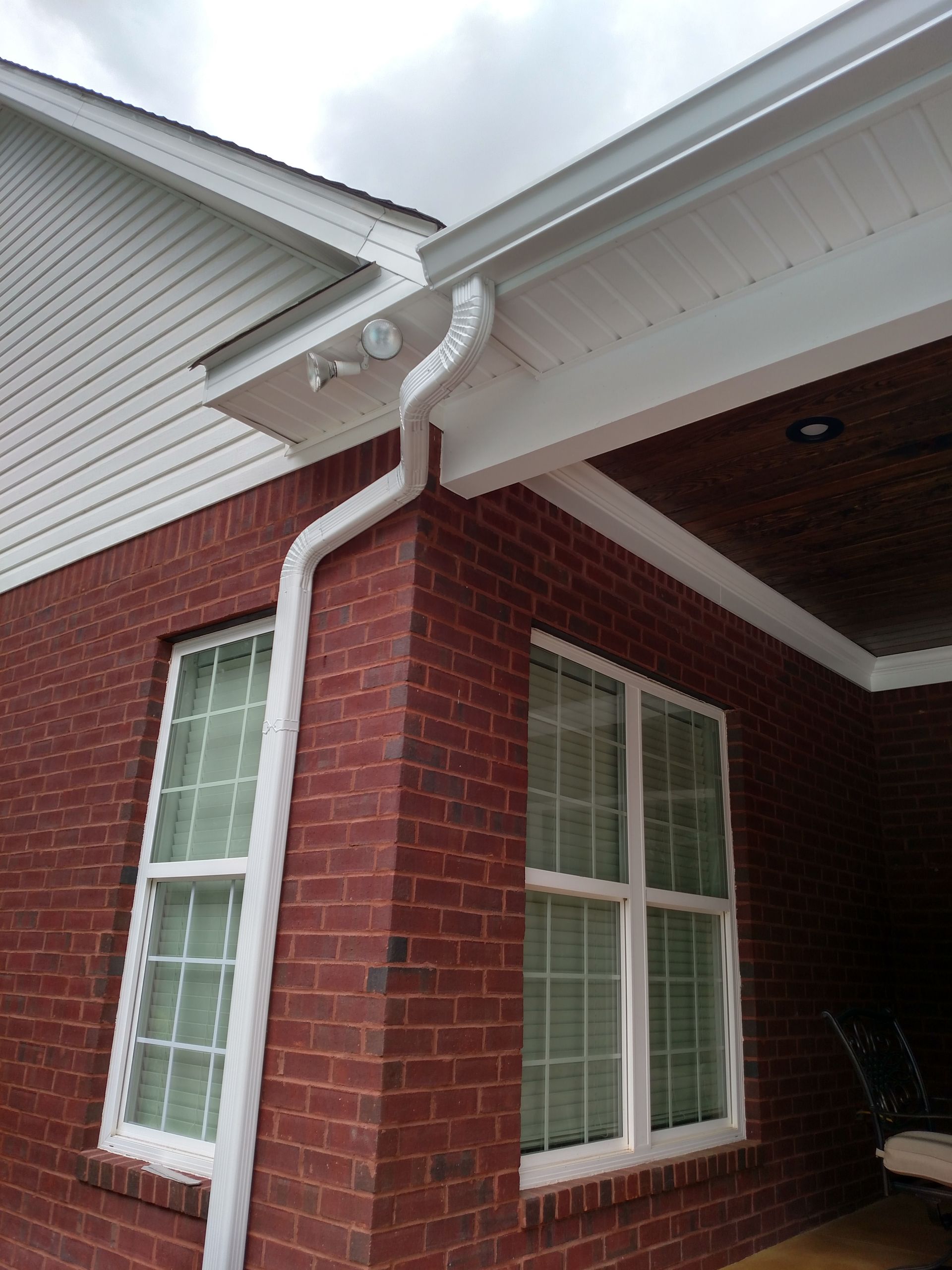Red brick building corner with white gutters, windows, and siding under a cloudy sky.