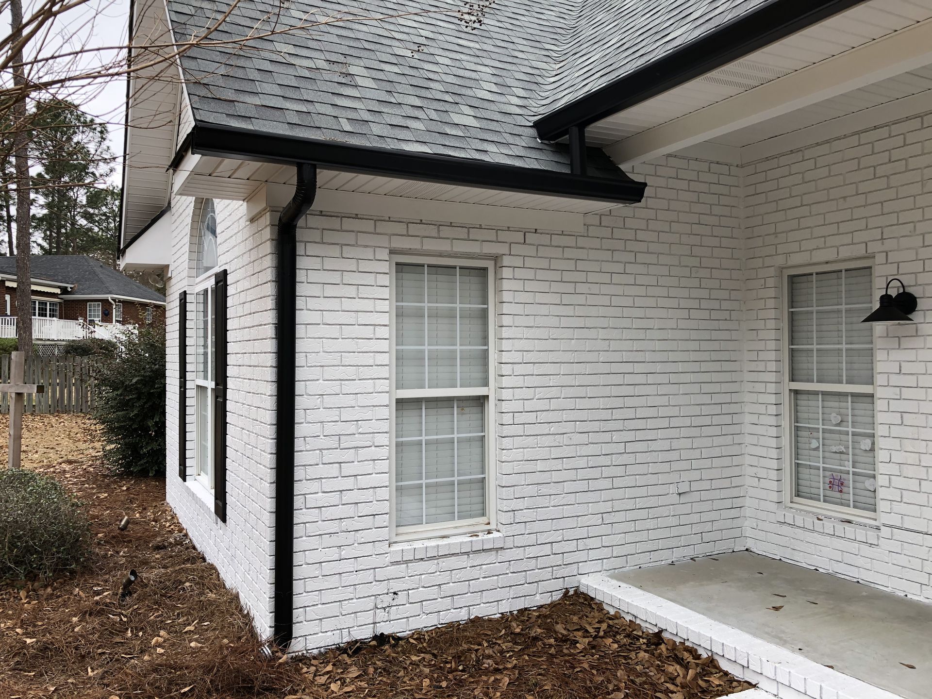 White brick house with black gutters and trim, two windows, and dark shutters.
