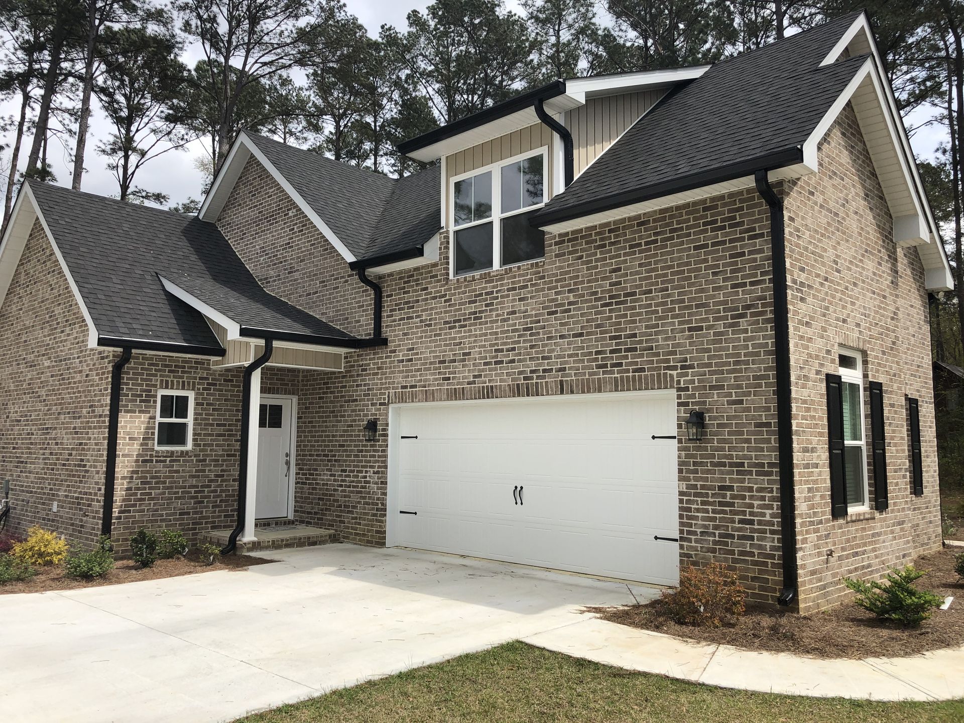 Brick two-story house with a white garage door, black roof, and black trim.
