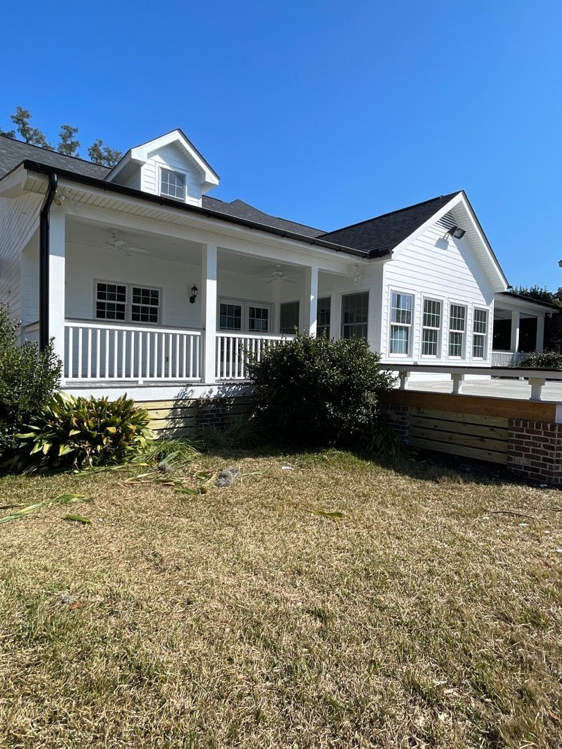 White house with a porch and dark roof against a clear blue sky. Dry, brown grass in the foreground.