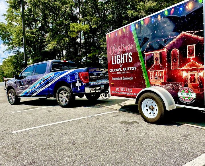 Two trucks are parked next to a trailer with christmas lights on it.