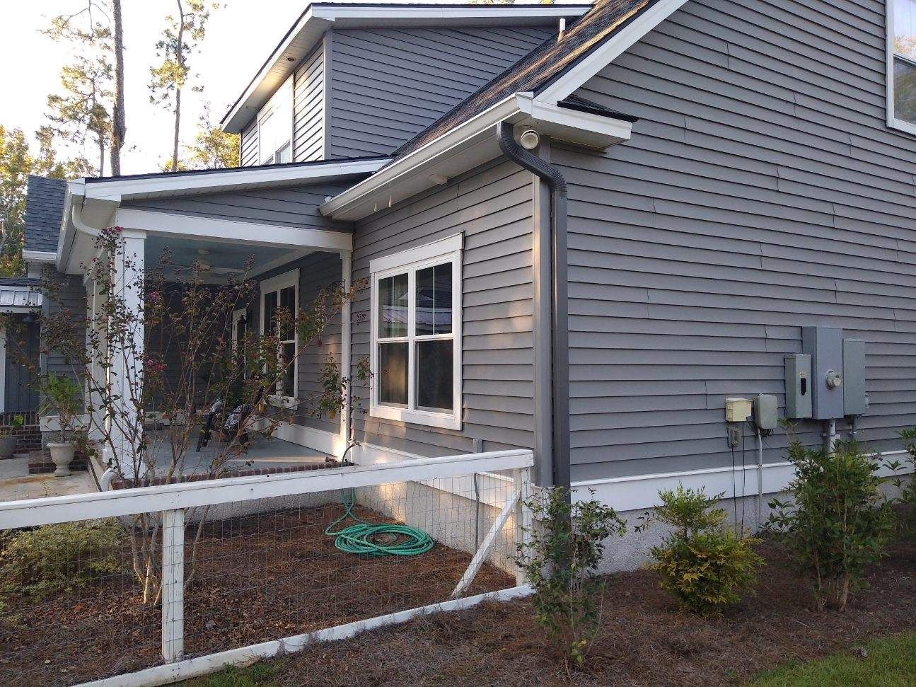 Gray house with white trim, porch, and a small fence in front.