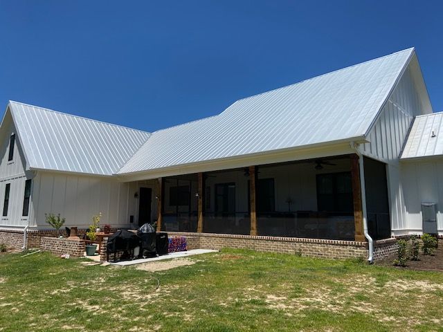 White farmhouse with metal roof, porch, and clear blue sky.