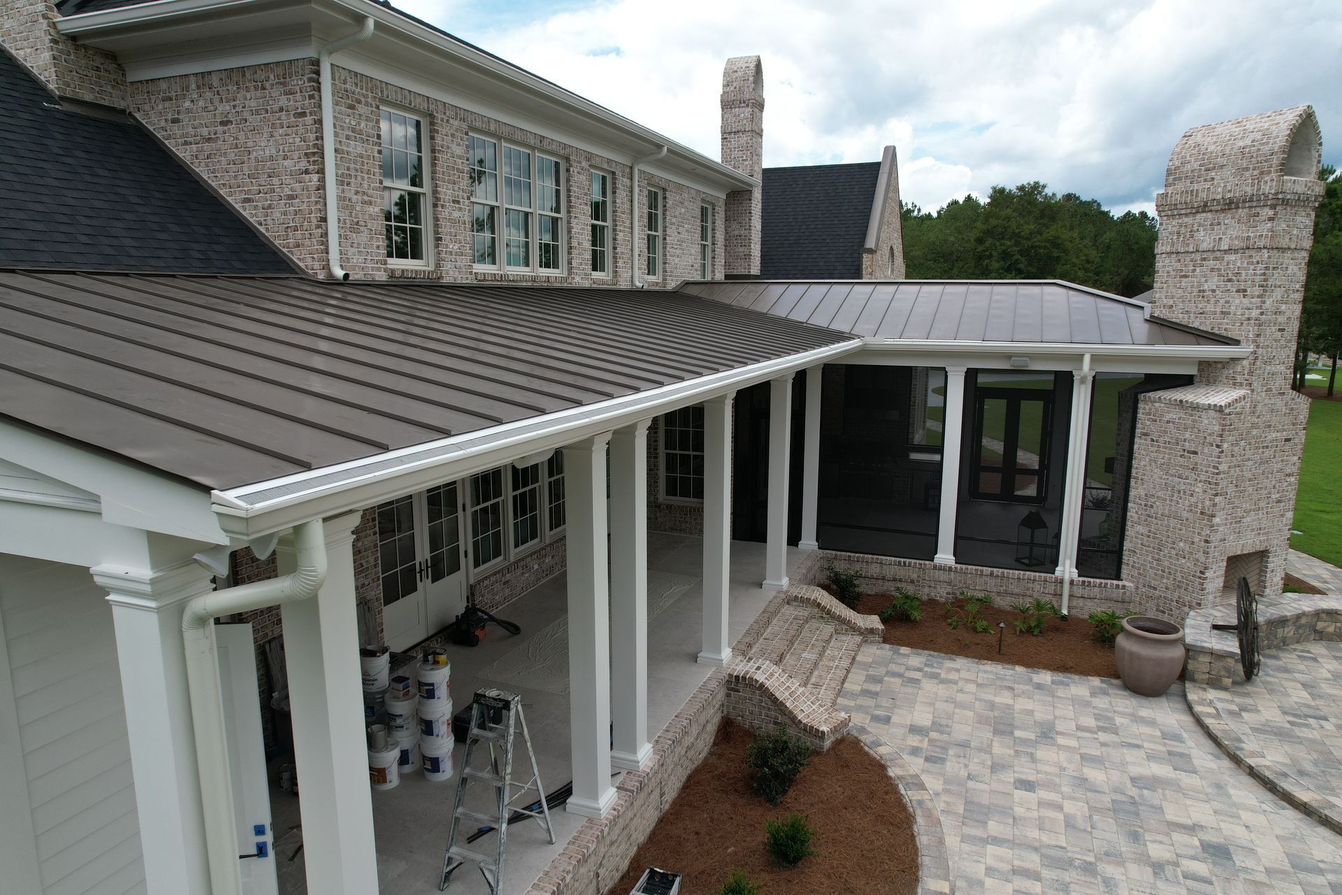 Two-story brick house with a dark metal roof and a screened-in porch with a stone patio.