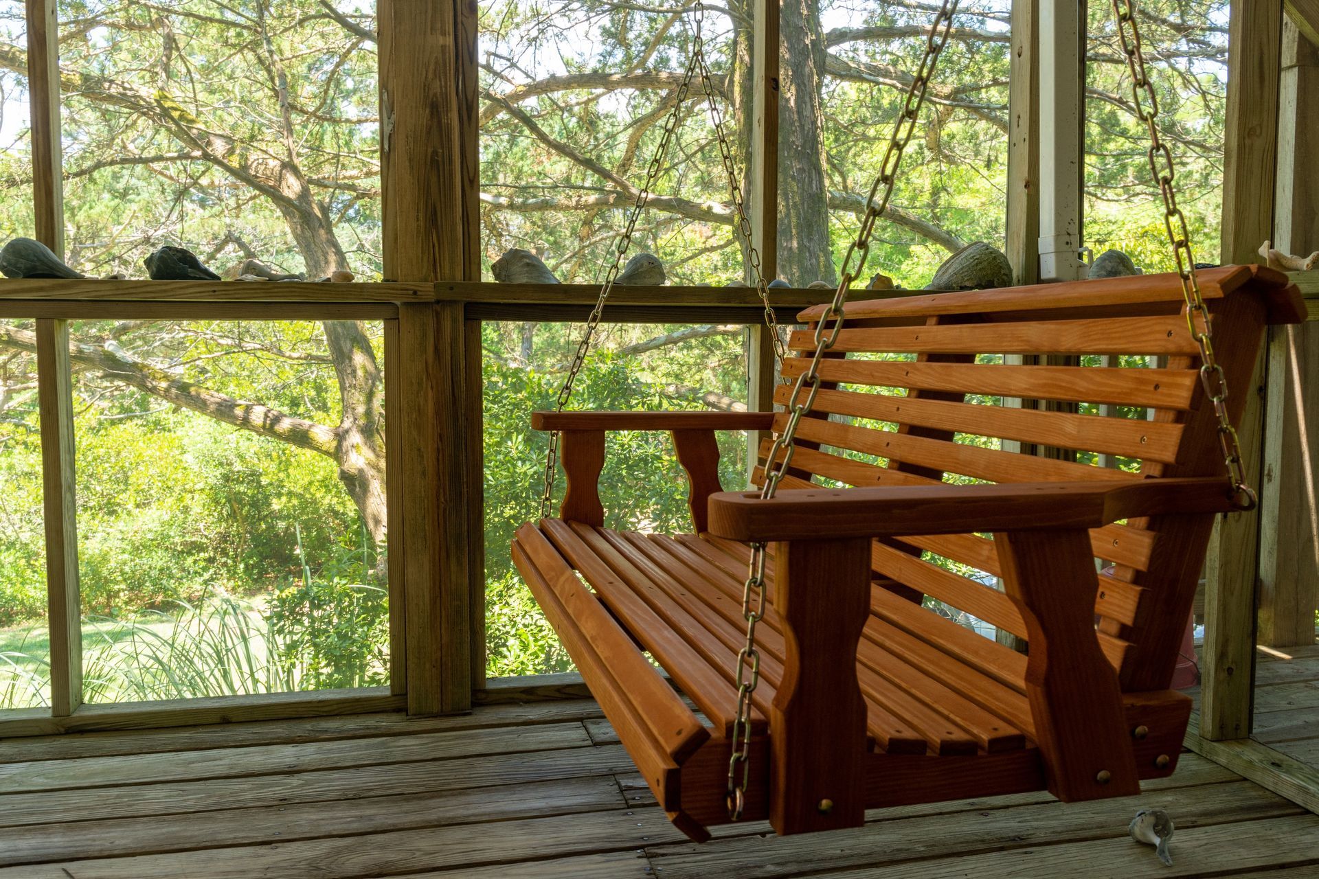 Wooden porch swing, brown, hanging from chains, overlooking trees.