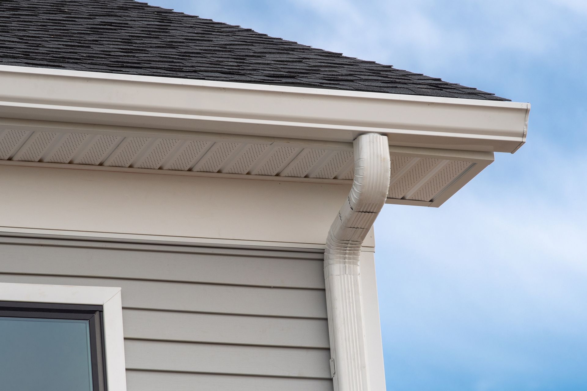 White gutters and downspout on a house with gray siding and dark roof.