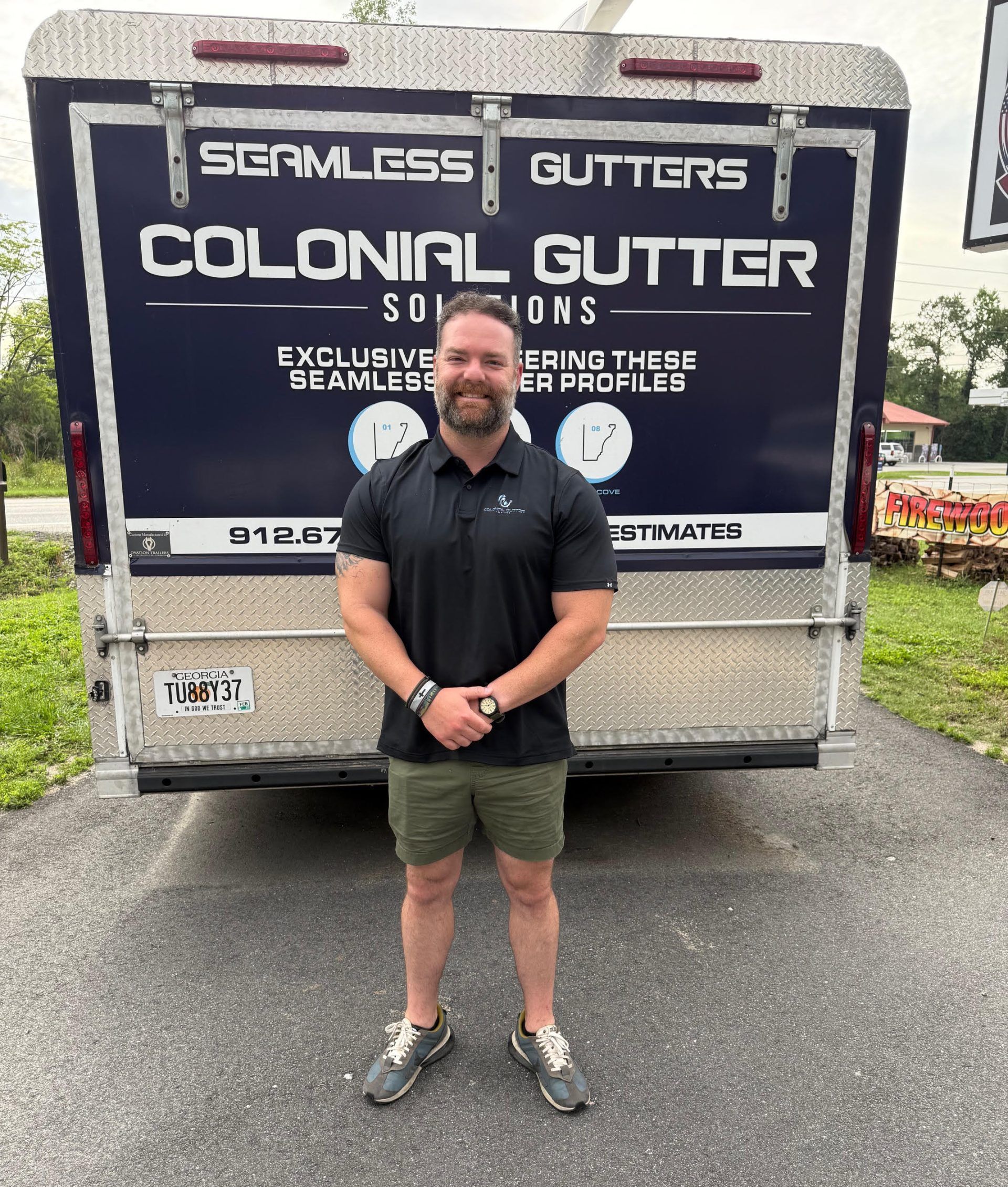 Man in shorts stands in front of a Colonial Gutter Solutions trailer.