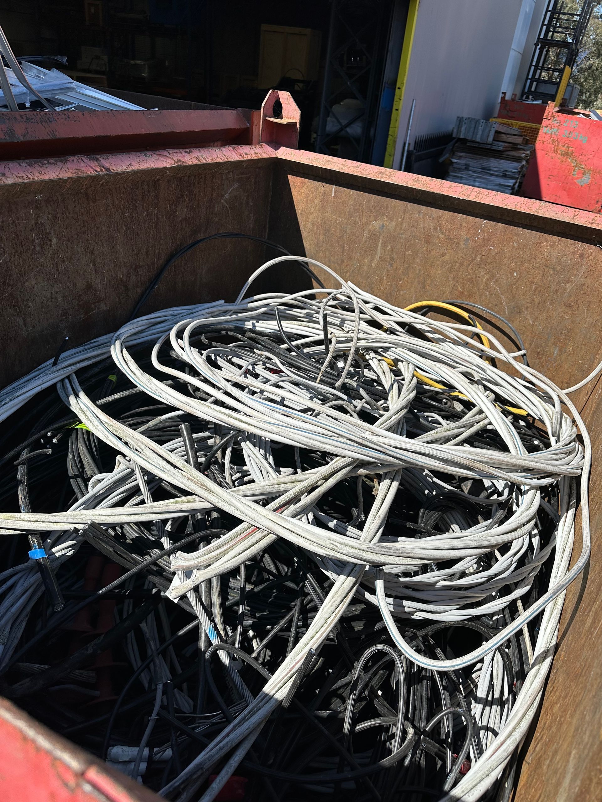 Pile of gray and black electrical wires inside a rusty red metal bin.