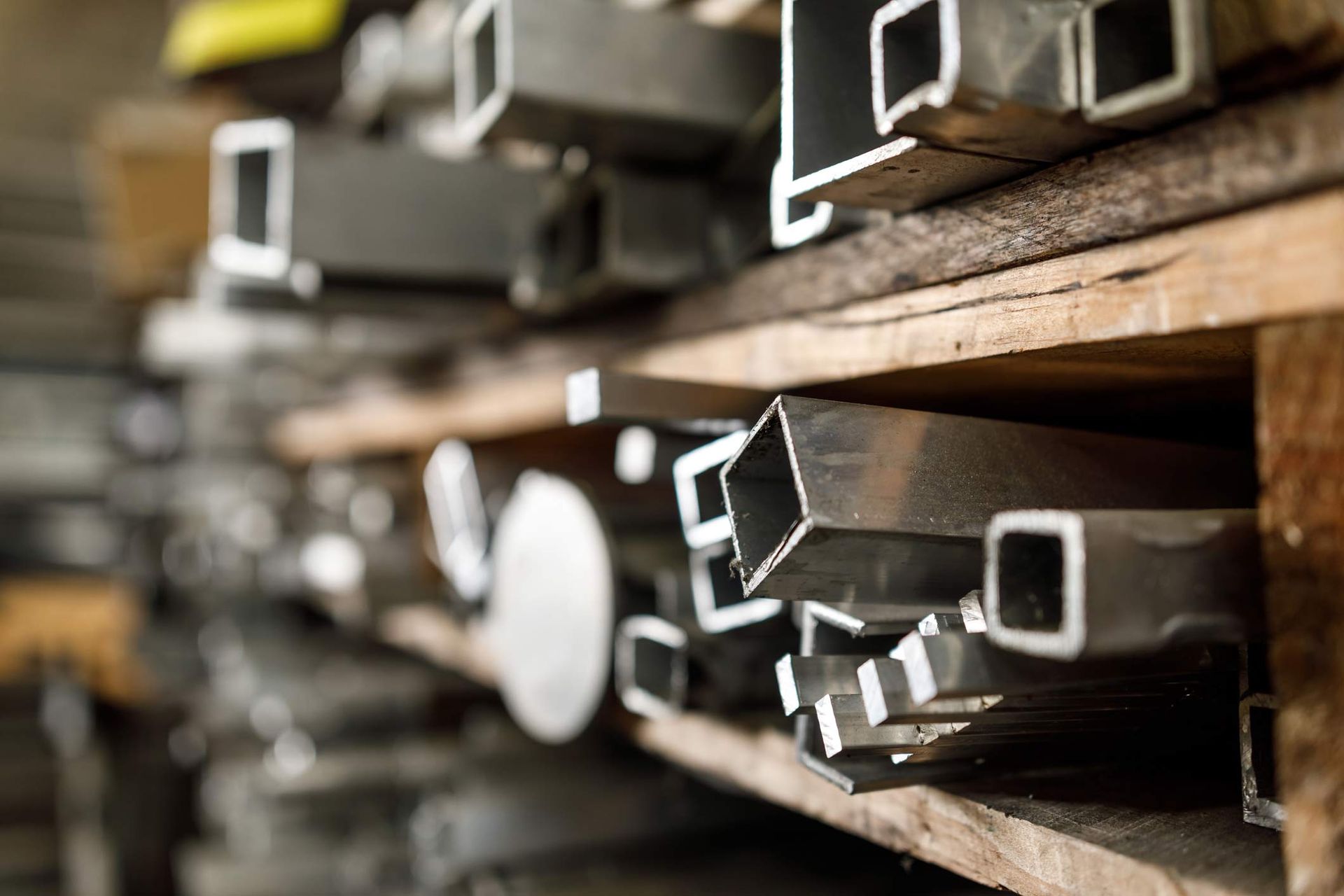 Metal square tubes on a wooden shelf in a storage space.