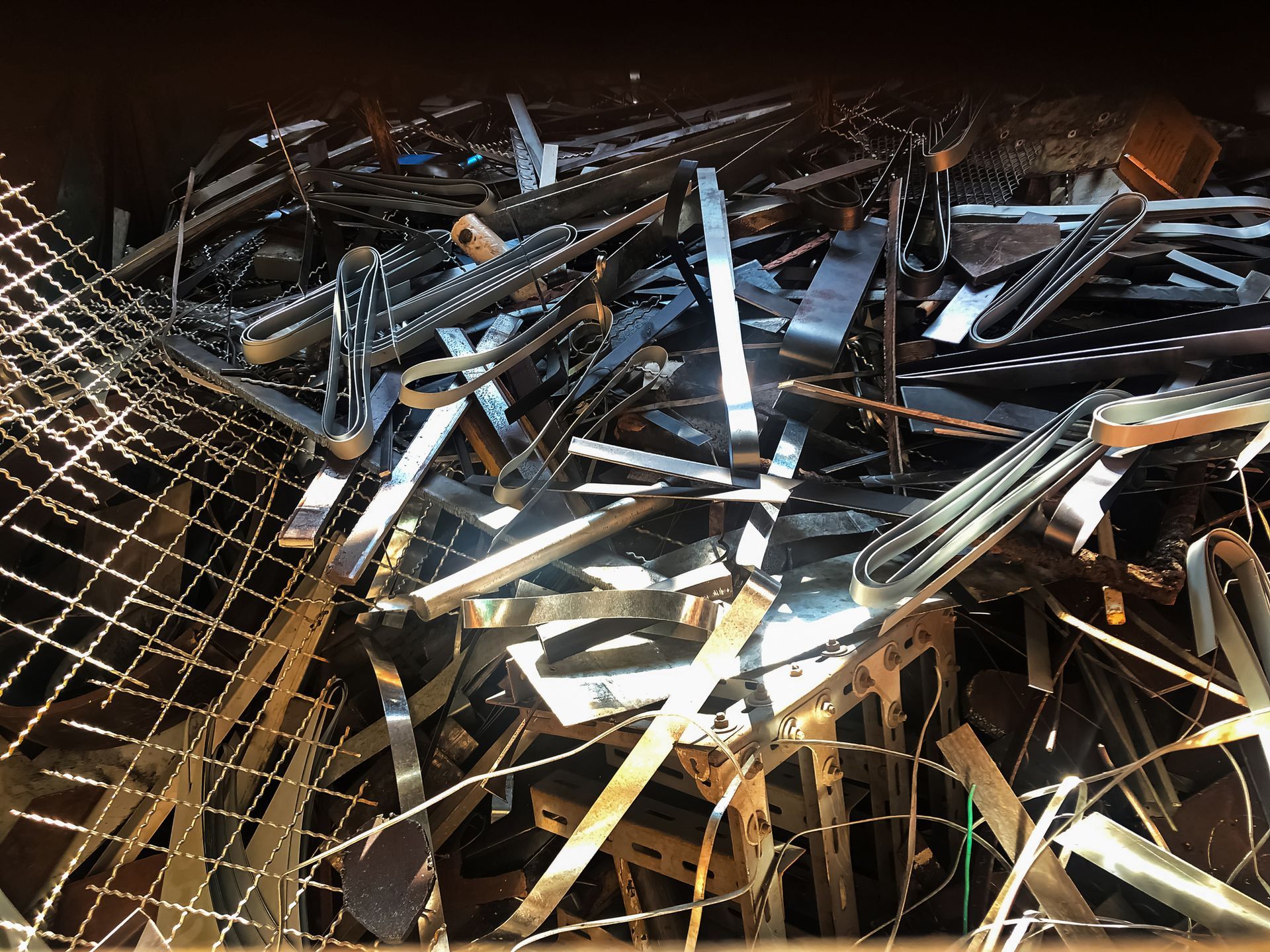 Pile of shiny, metal scrap pieces in a bin, including strips, bars, and wire mesh.