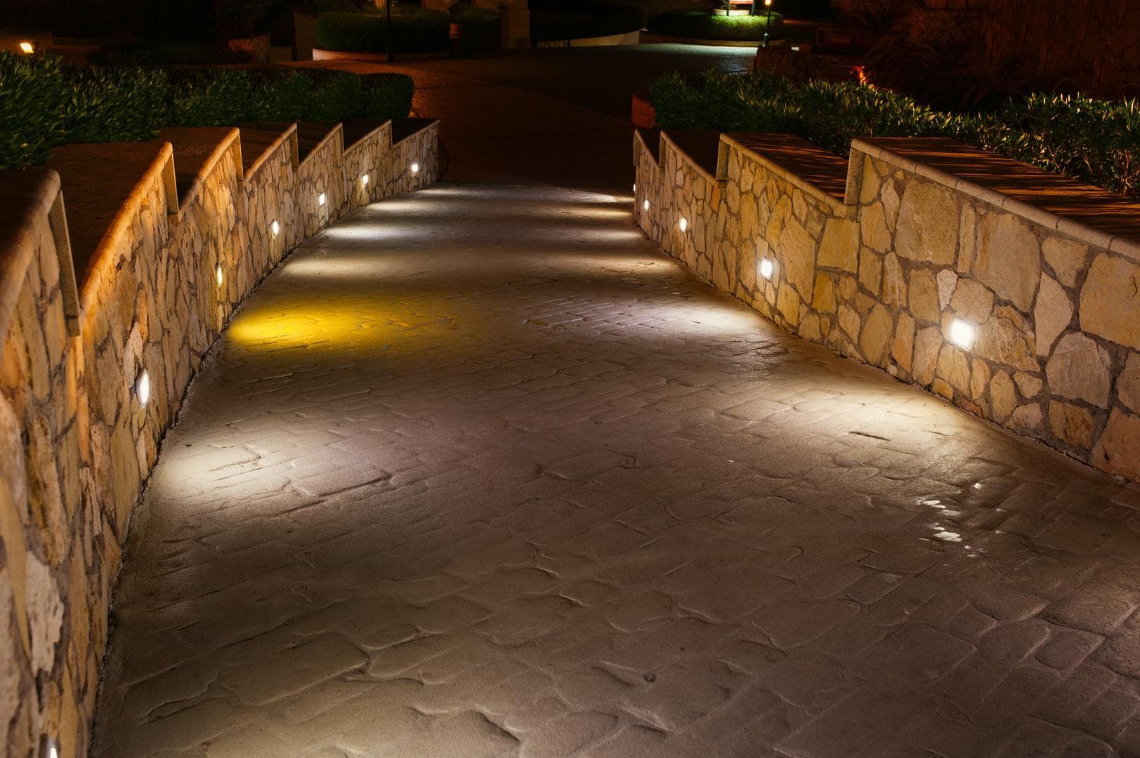 A stone walkway with lights on the side of it at night.