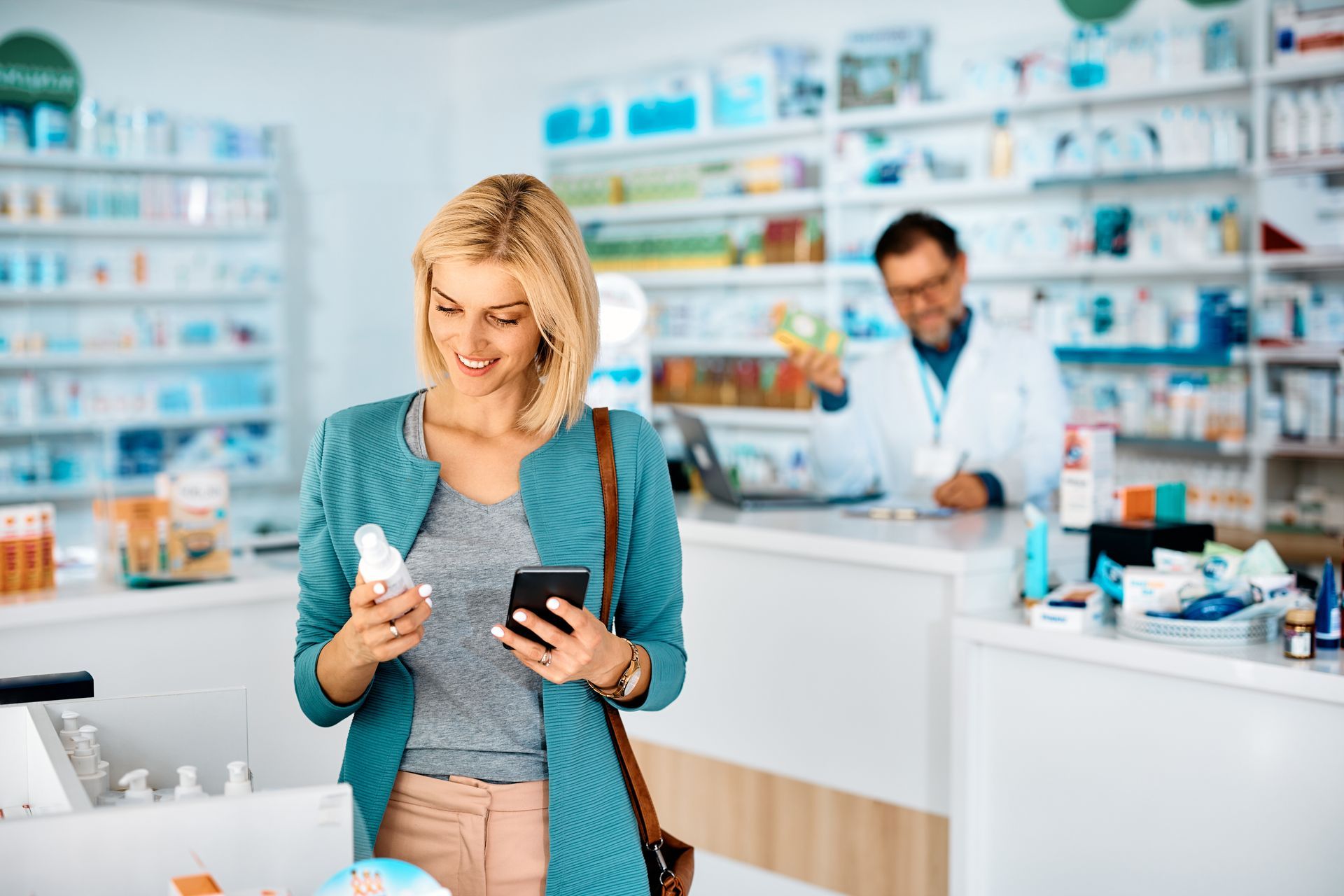 a Pharmacist is Using a Laptop Computer in a Pharmacy While Holding a Bottle of Pills — Warners Bay Pharmacy In Warners Bay, NSW
