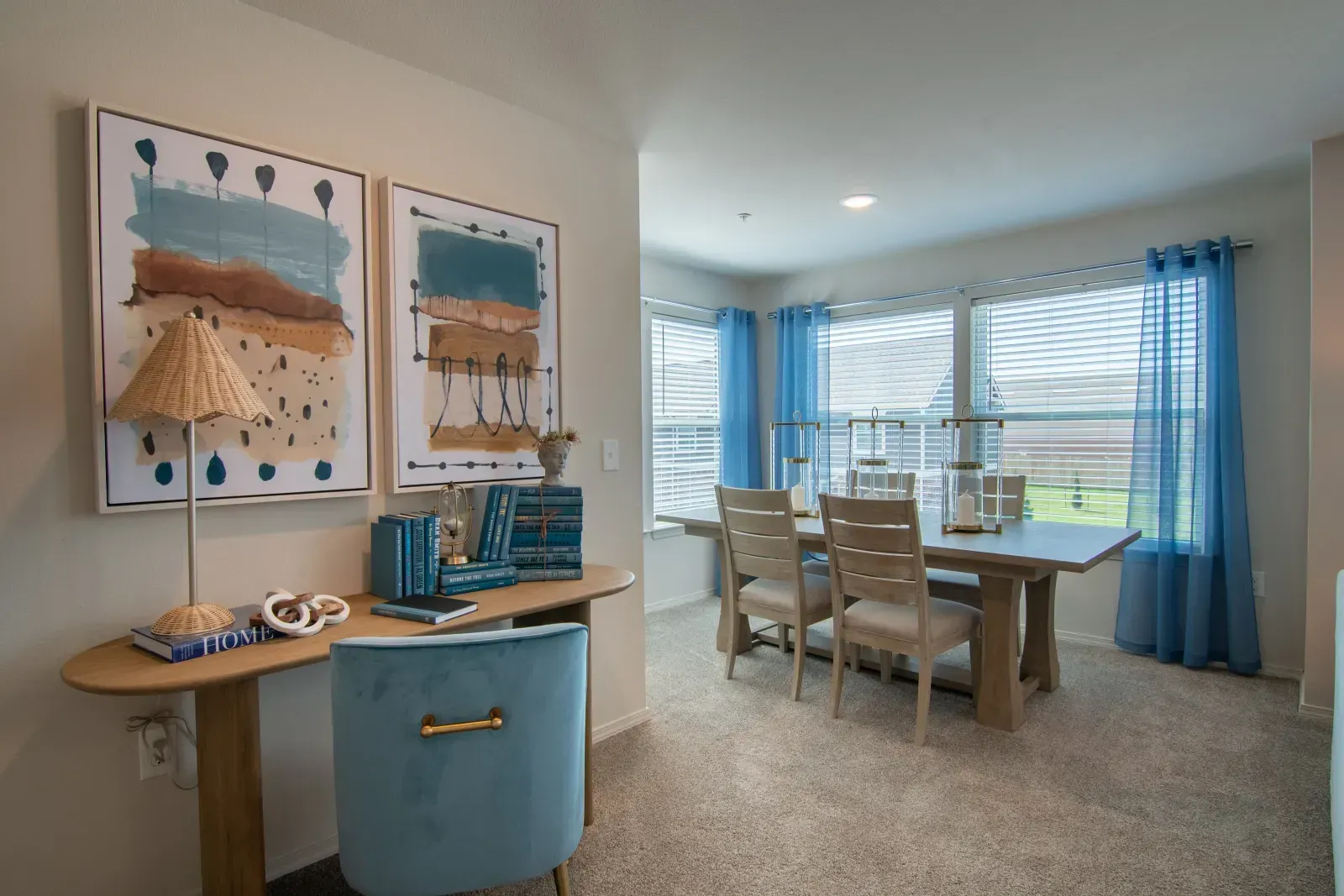 Sunlit dining area in an apartment featuring a light wood table, chairs, and blue window curtains.