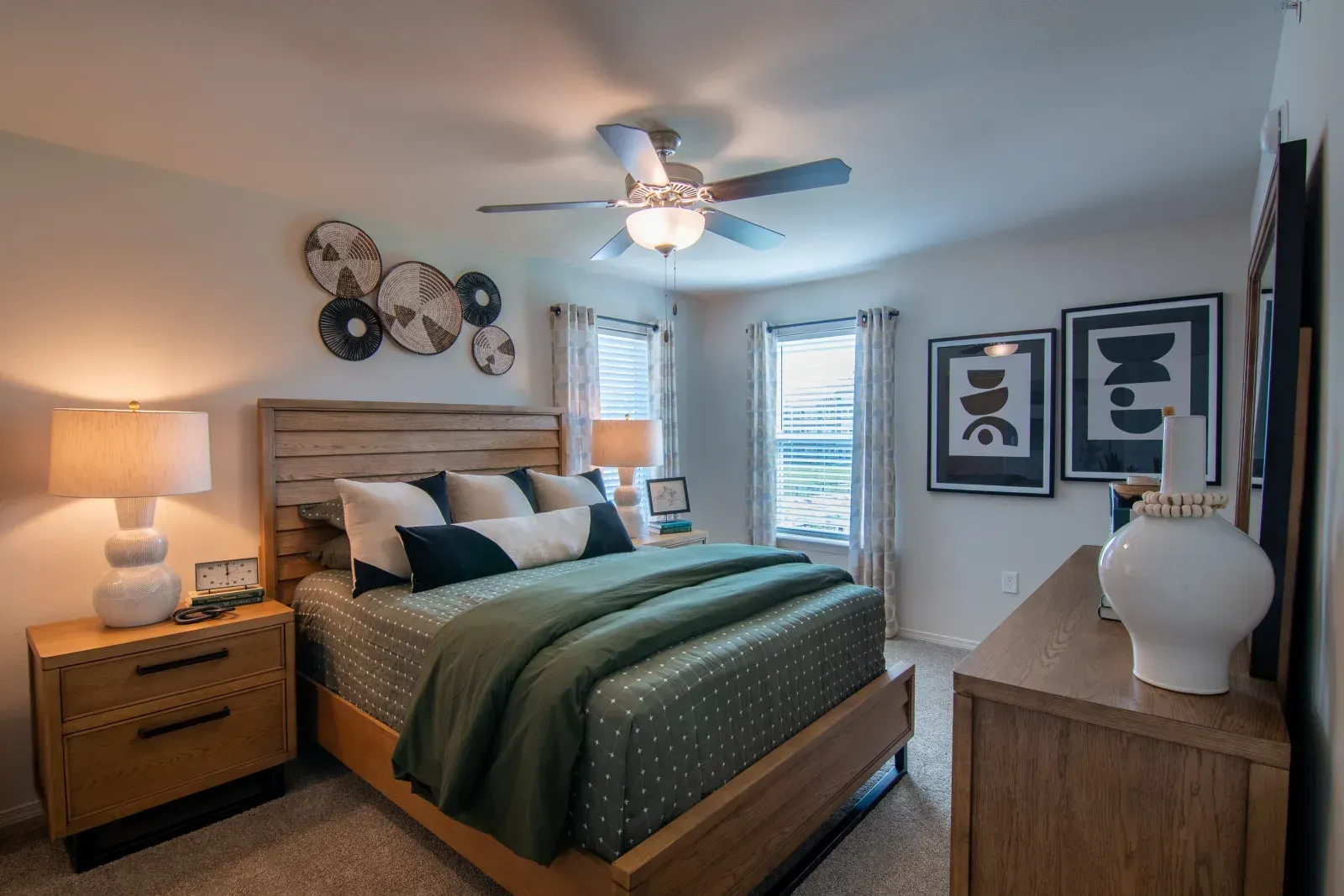 Cozy apartment bedroom featuring a wooden bed, two nightstands, ceiling fan, and wall art.