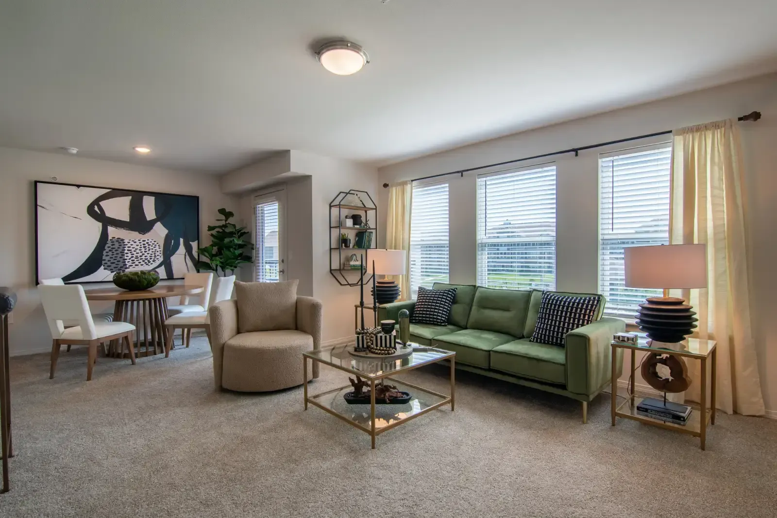 Bright living room with a green sofa, glass coffee table, and large windows with blinds.