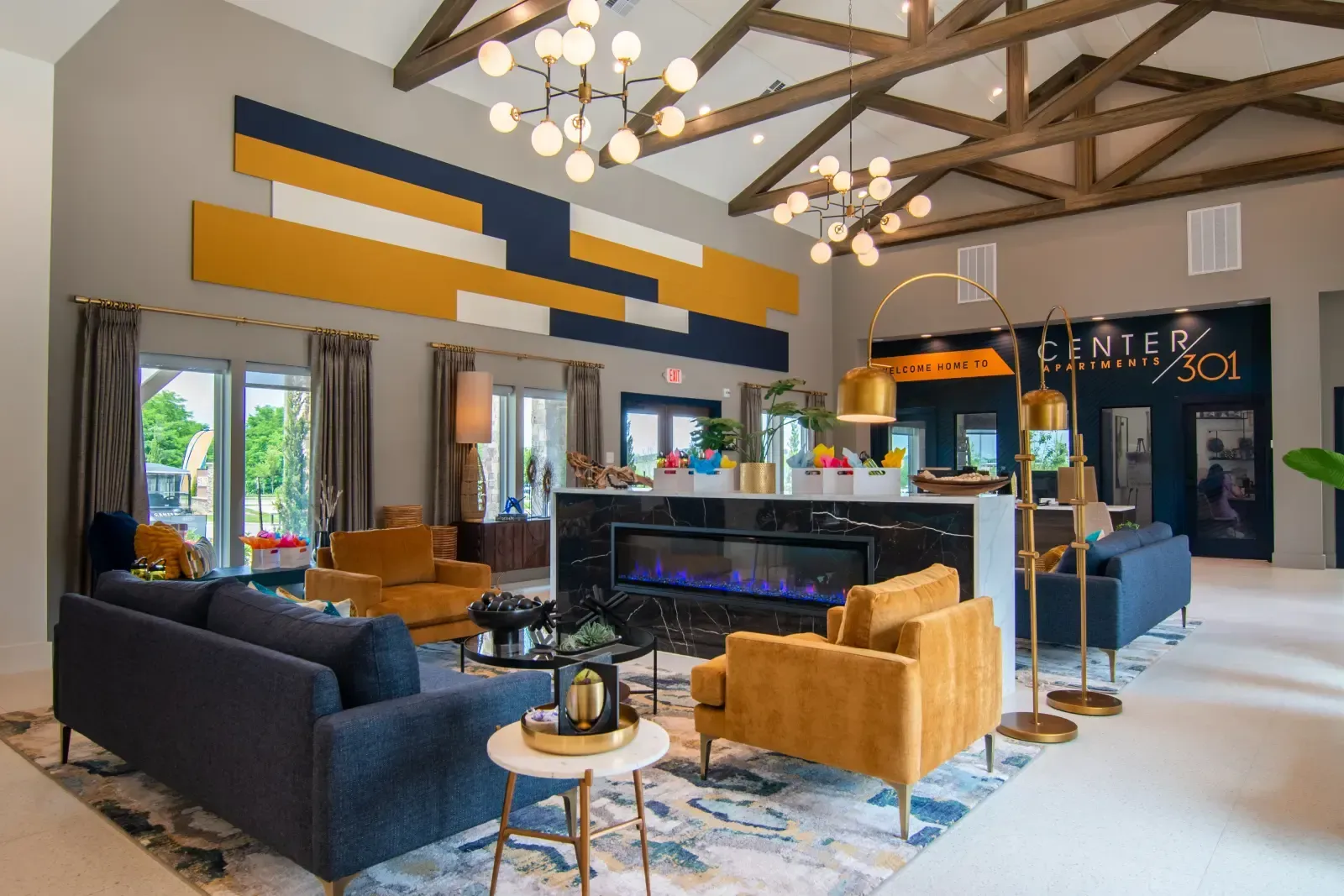 Modern apartment community lobby with blue-yellow geometric wall art, seating, and a marble fireplace.