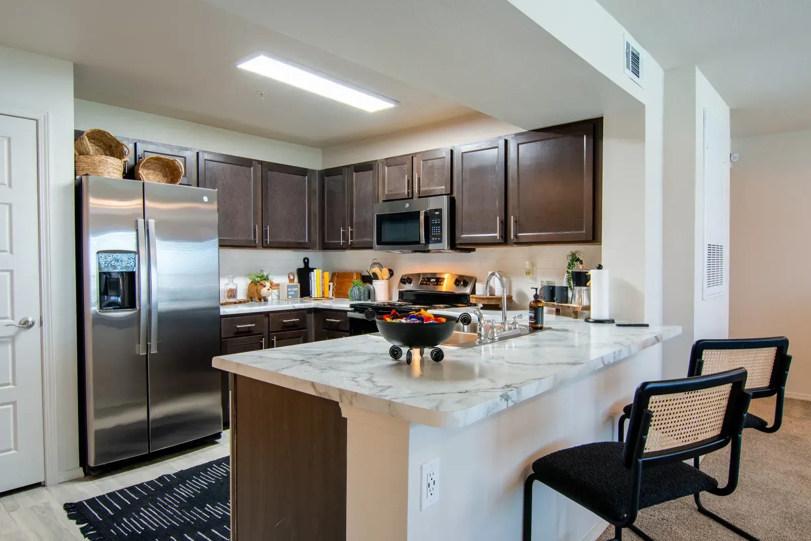 Kitchen in a modern apartment with dark cabinets, stainless appliances, and a marble island.