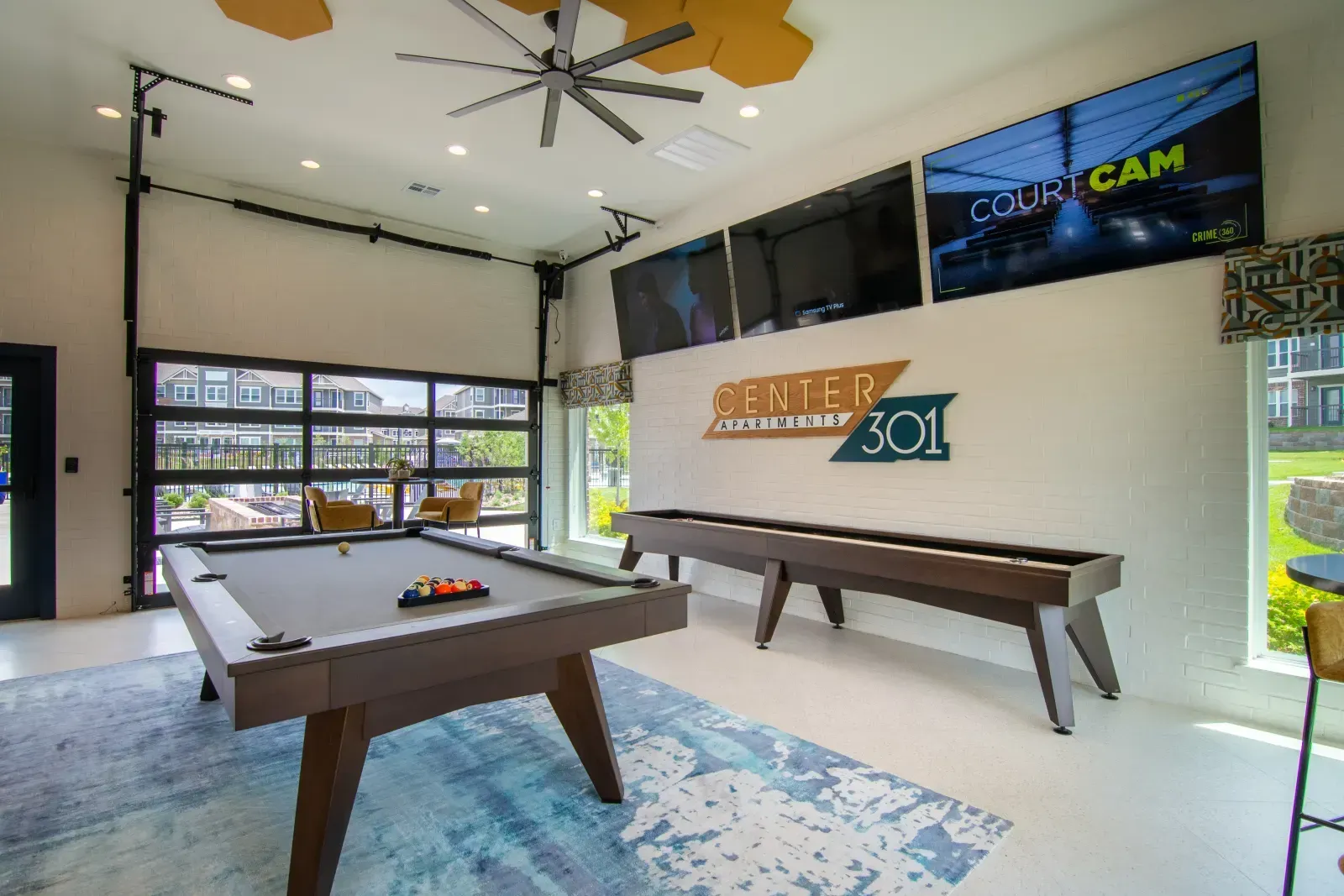 Indoor community lounge with a pool table, wall-mounted TVs, and seating.