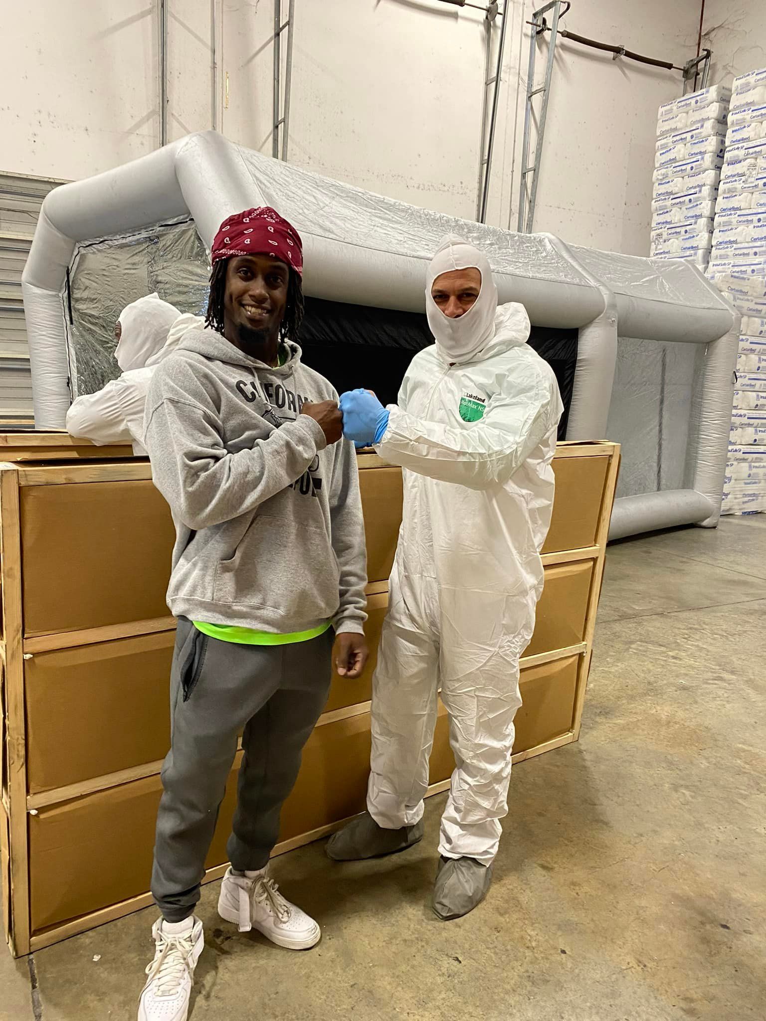 Two men in protective suits are standing next to each other in a warehouse.