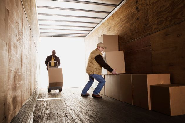 Due persone caricano scatole di cartone su un camion, una delle quali utilizza un carrello.