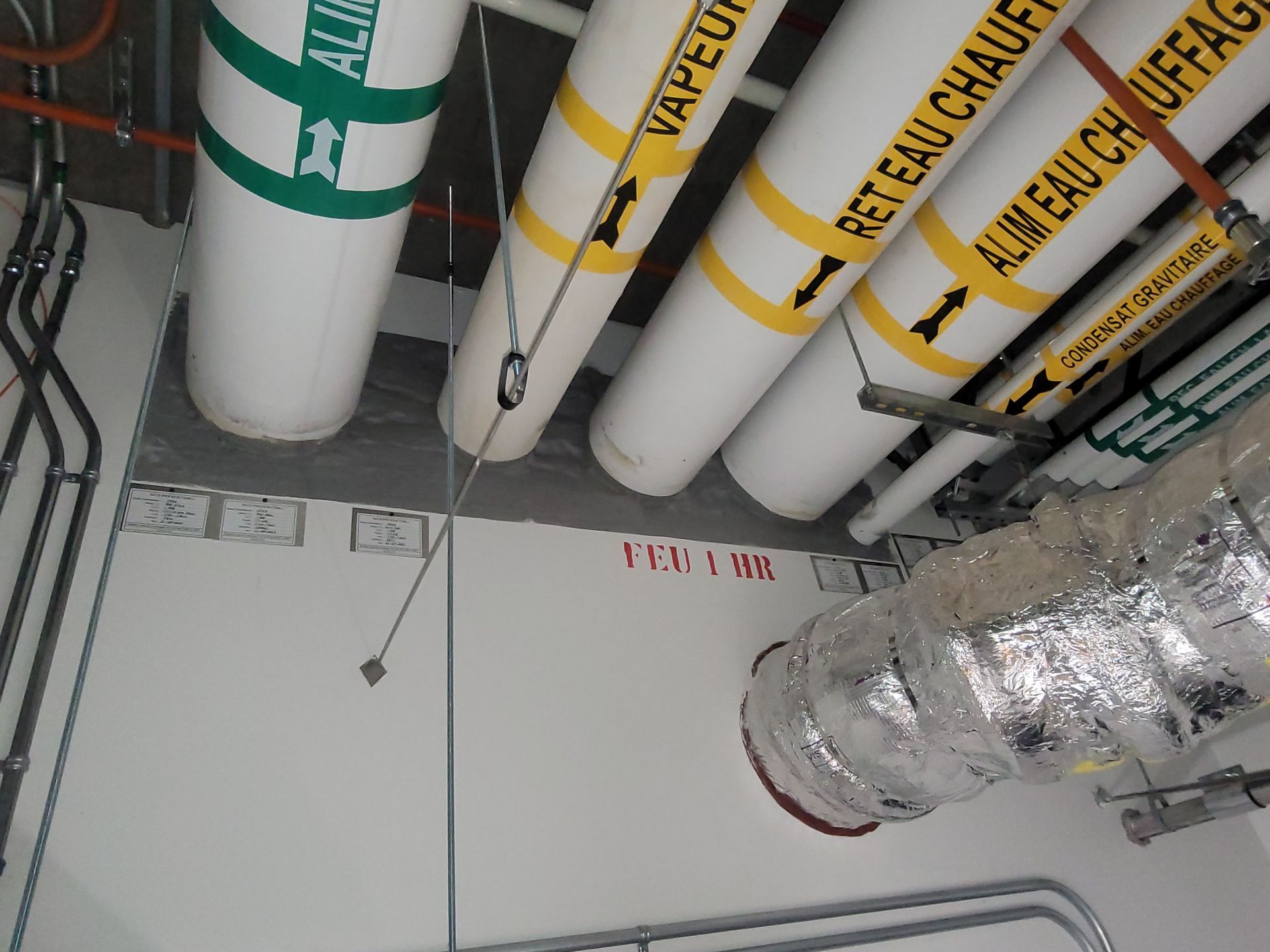 Un tas de tuyaux suspendus au plafond avec un sur lequel est écrit vapeu