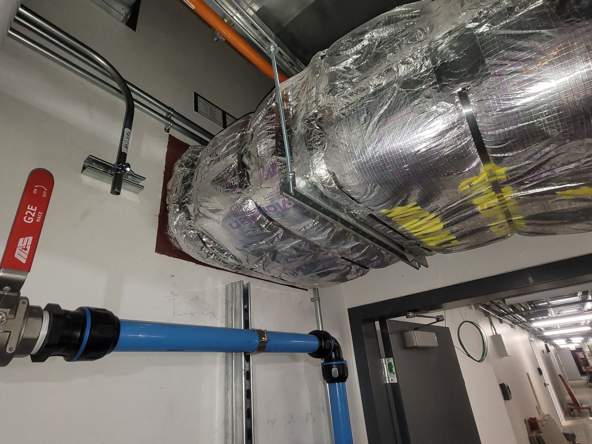 Une valve rouge est suspendue au plafond à côté d'un tuyau bleu.