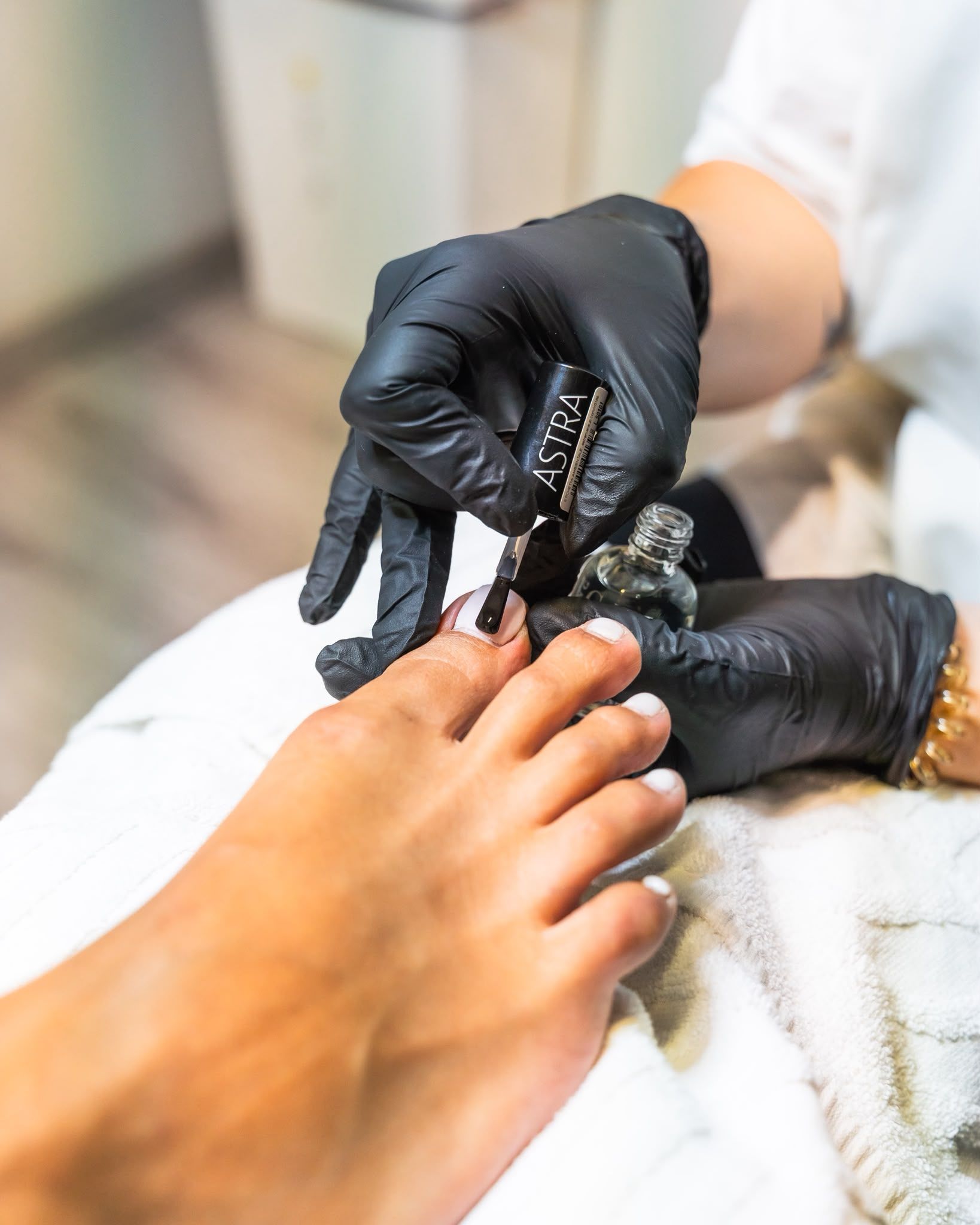 Mani guantate di nero che dipingono di nero un'unghia del piede in un salone di manicure.