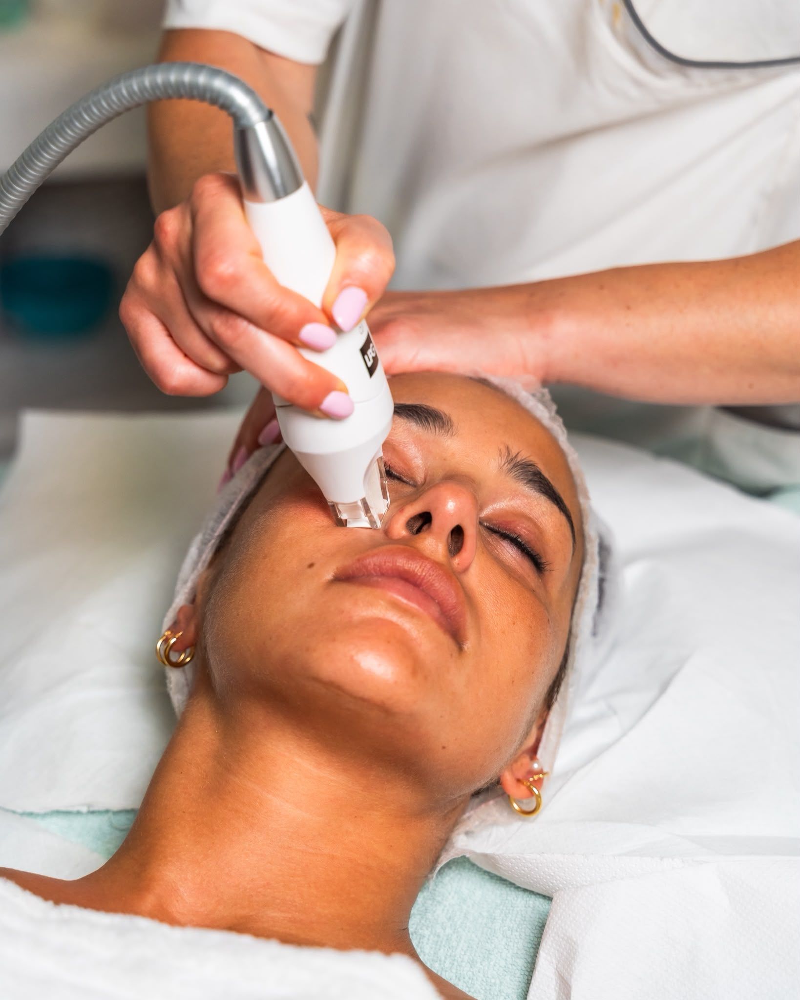 Trattamento viso con dispositivo portatile applicato a una donna sdraiata su un lettino da spa.
