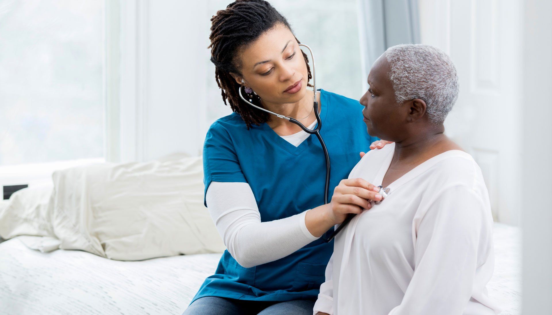 A nurse is listening to an older woman 's heartbeat with a stethoscope.
