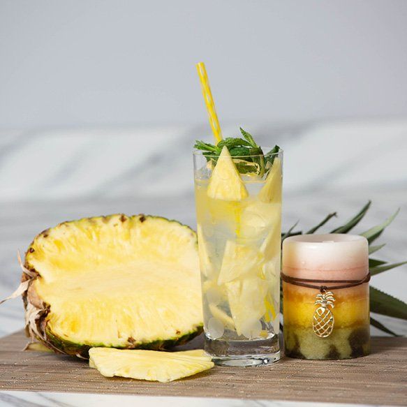 A glass of pineapple juice next to a pineapple and a candle
