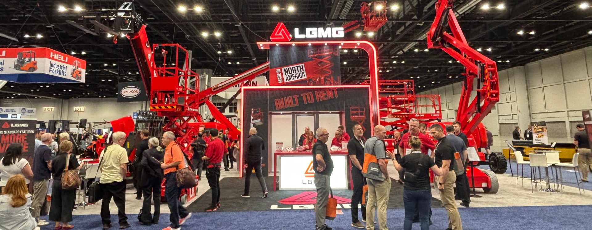 LCMG equipment display at a trade show with people gathered around. Red machinery, blue carpet, and a banner are visible.