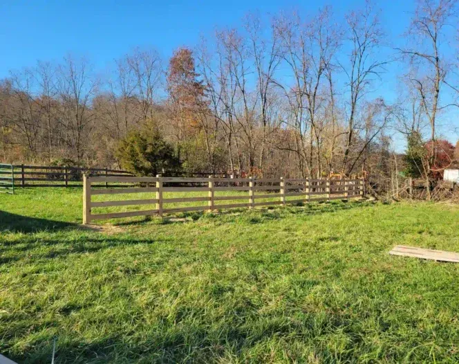 A wooden fence surrounds a grassy field with trees in the background.