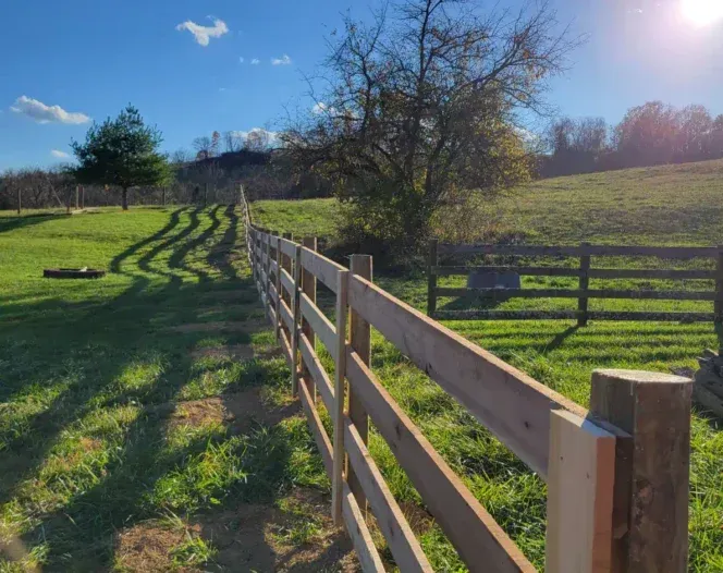 A wooden fence surrounds a grassy field on a sunny day