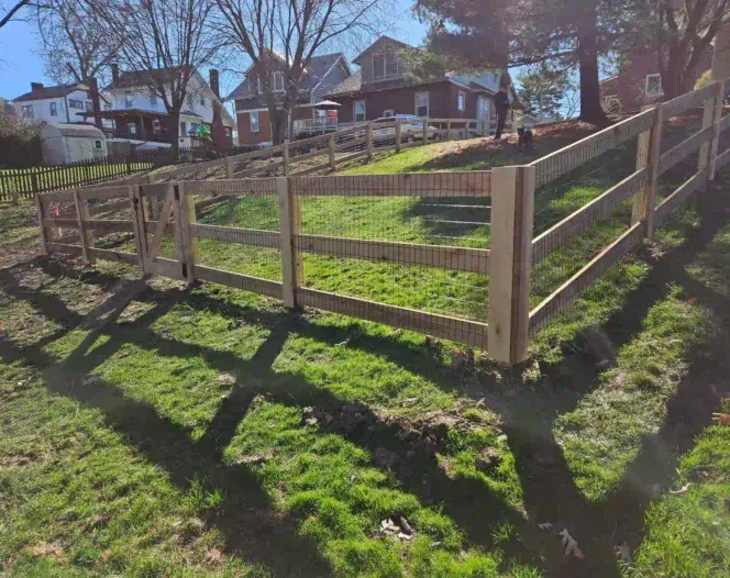 A wooden fence surrounds a grassy field with houses in the background.