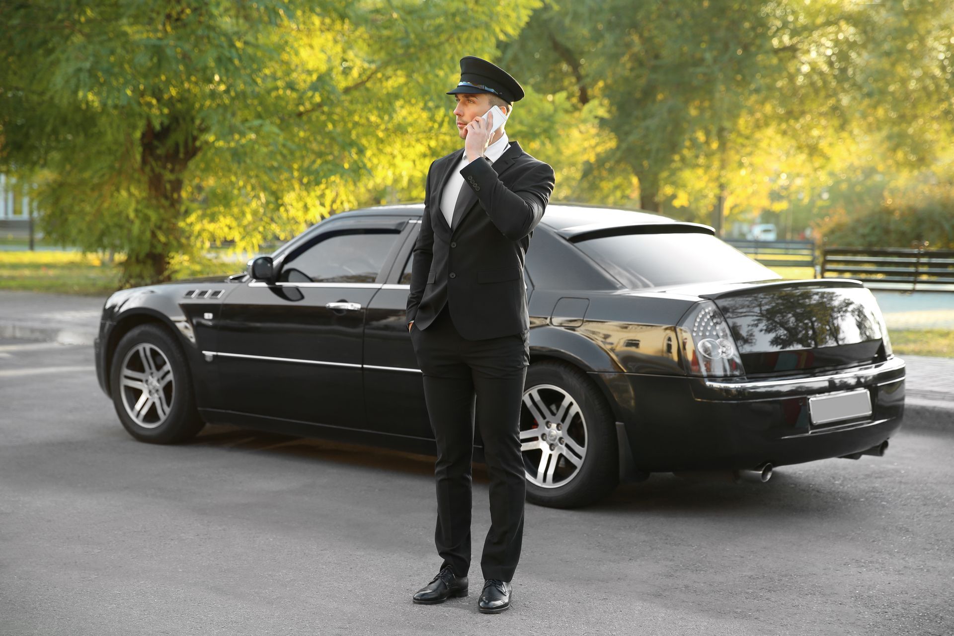 A man in a suit is talking on a cell phone in front of a black limousine.