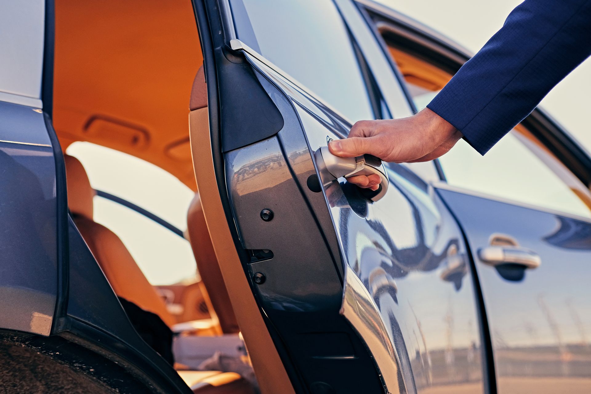 A man in a suit is opening the door of a car.