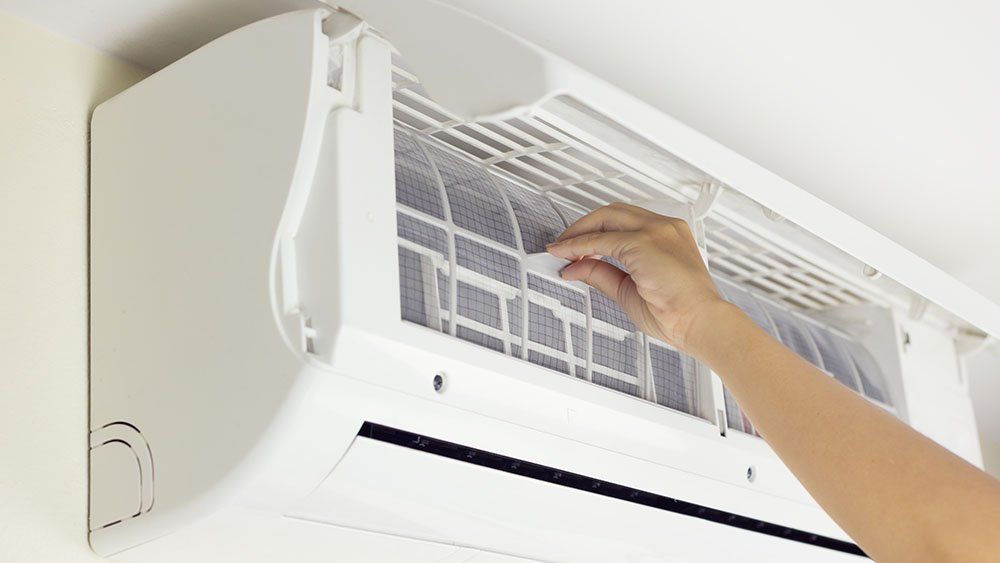 Hand adjusting the filter of a white wall-mounted air conditioner