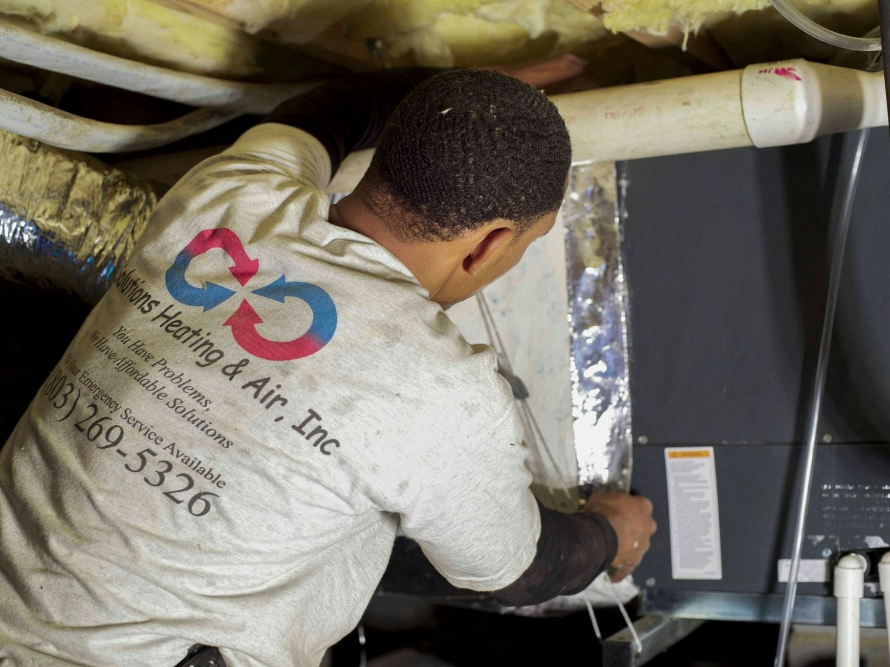 Technician inspecting HVAC unit in a cramped crawlspace under a house