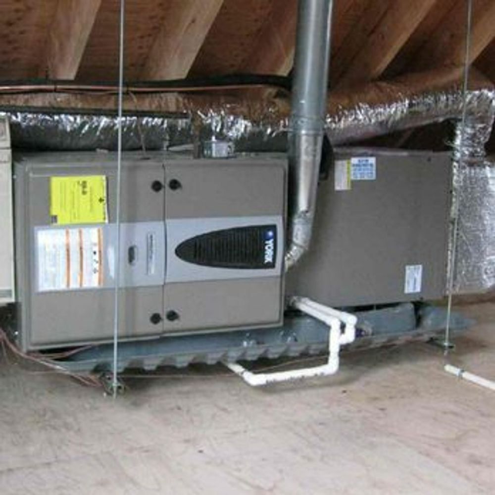 Attic HVAC units and ductwork installed under a sloped roof, with insulation and white PVC piping
