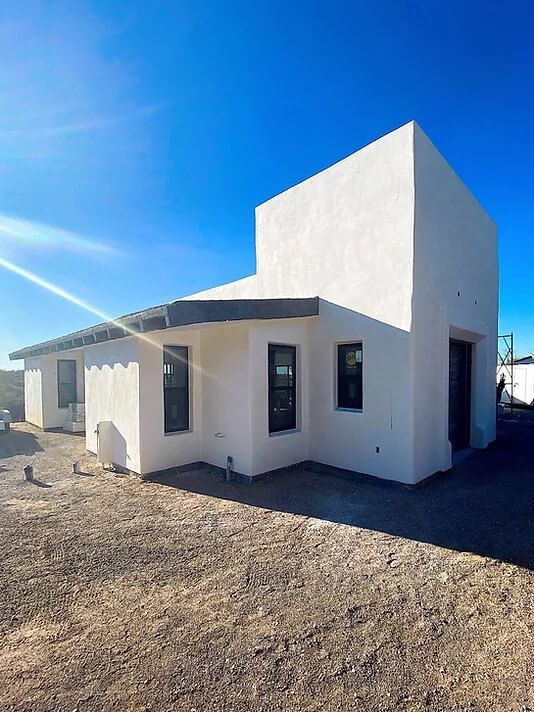 A white house with a lot of windows is sitting in the middle of a dirt field.