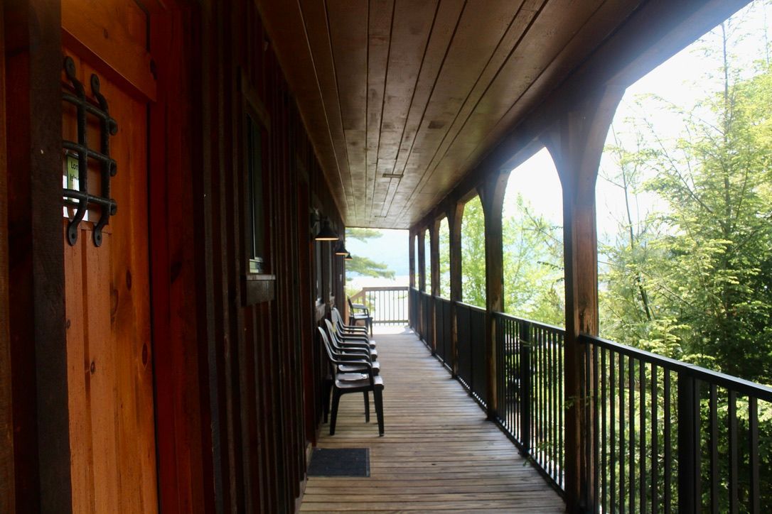 A long wooden hallway with chairs and a railing leading to a balcony.